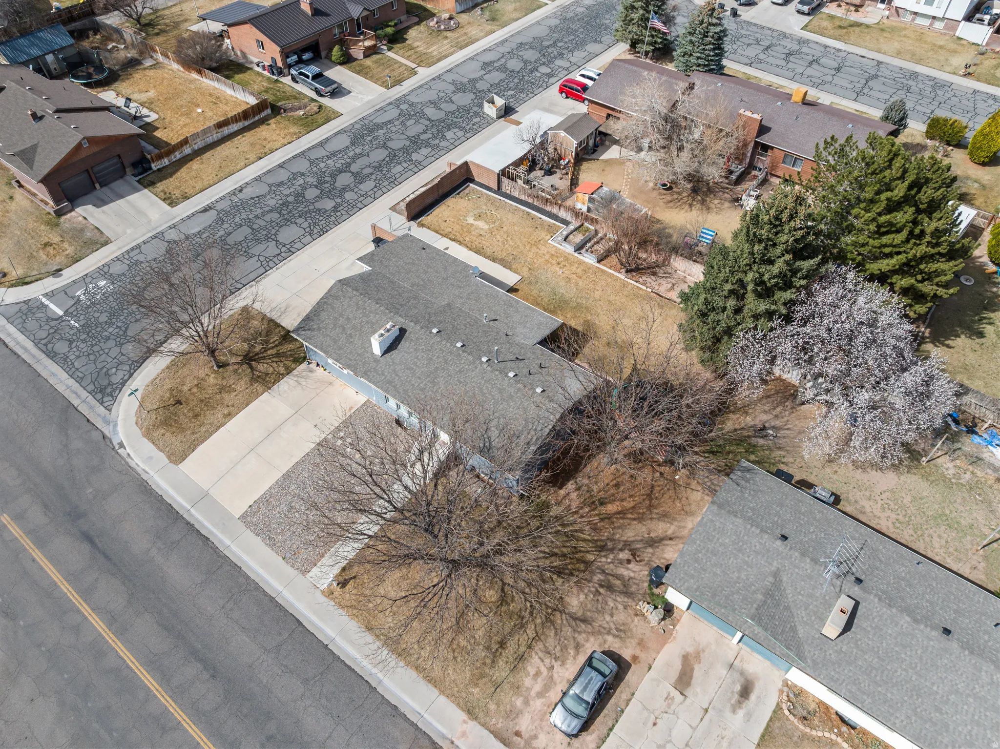 Aerial perspective highlighting the property with a gray shingle roof, a paved driveway, and established trees