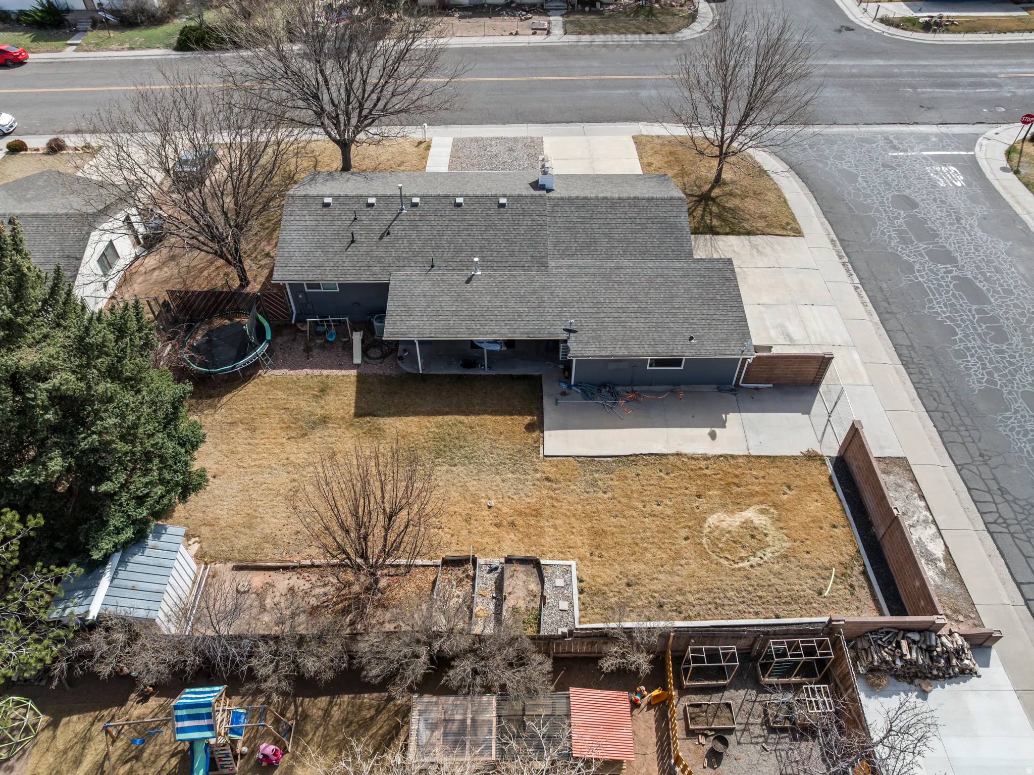 Corner lot property featuring a gray exterior, dark gray shingle roof, and an attached covered patio