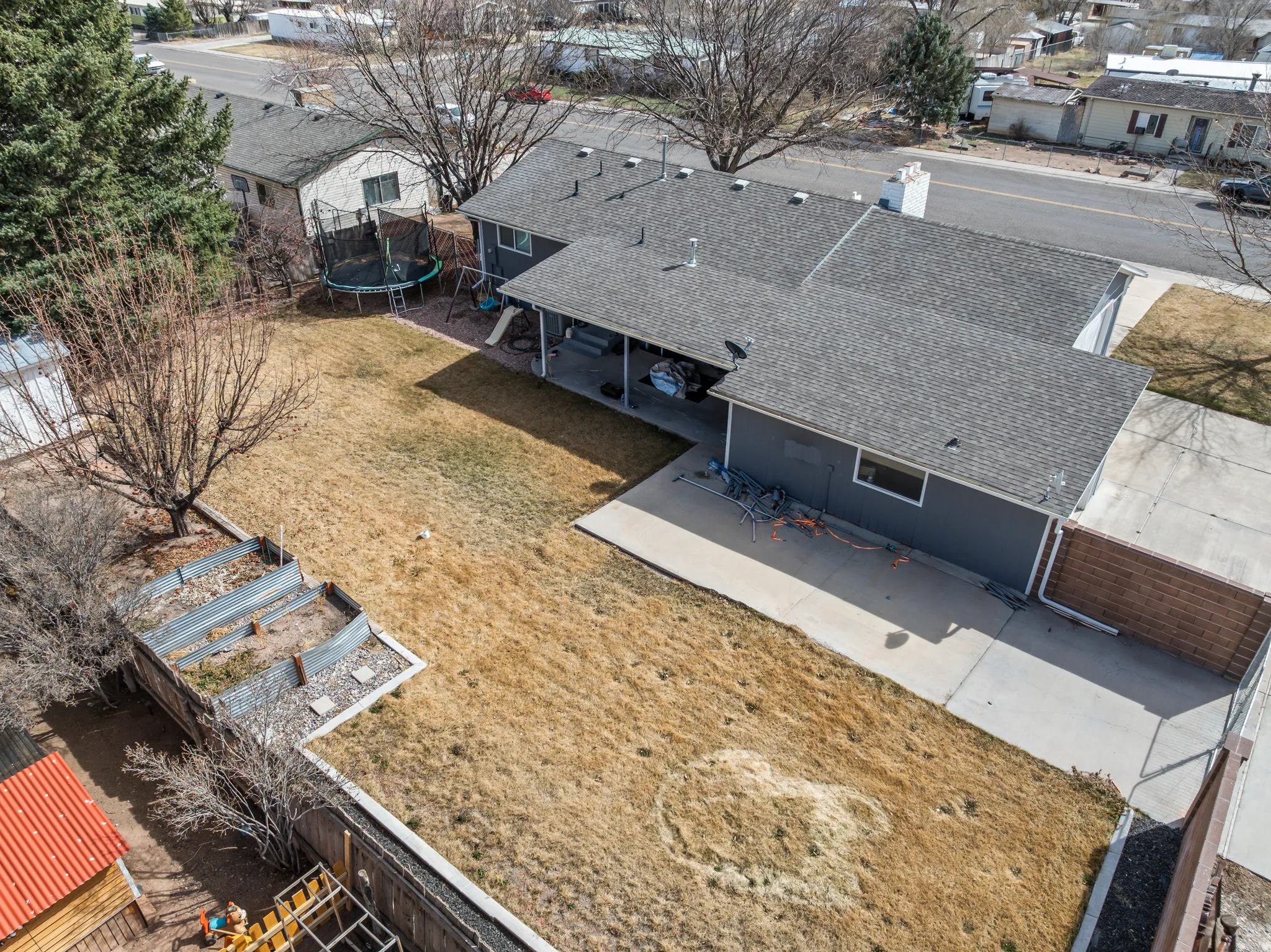 Expansive backyard featuring a large concrete patio, raised garden beds, and a perimeter fence