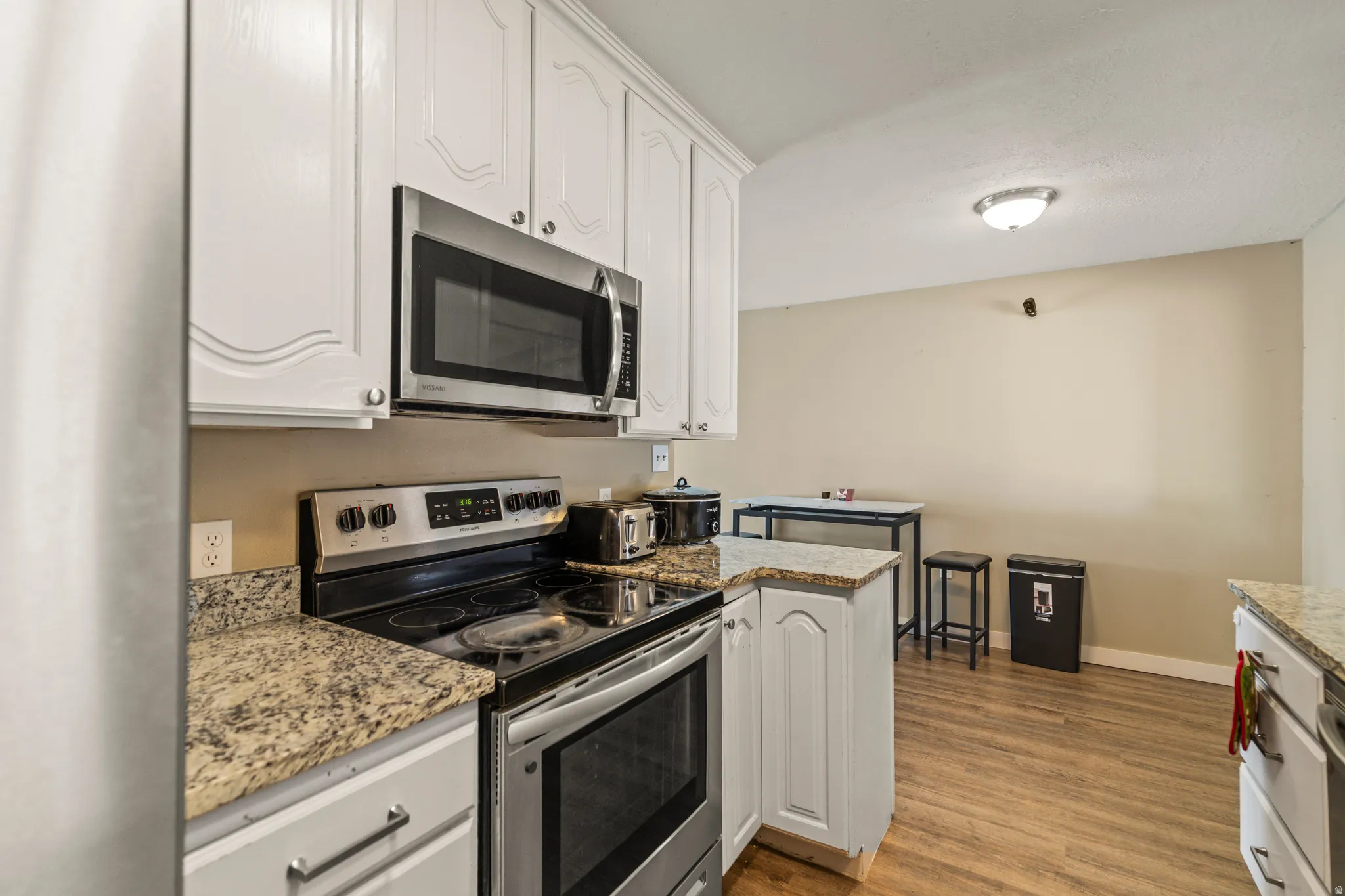 Kitchen featuring white cabinetry, stainless steel appliances including an oven range and microwave, granite-finish countertops, and wood-finish flooring