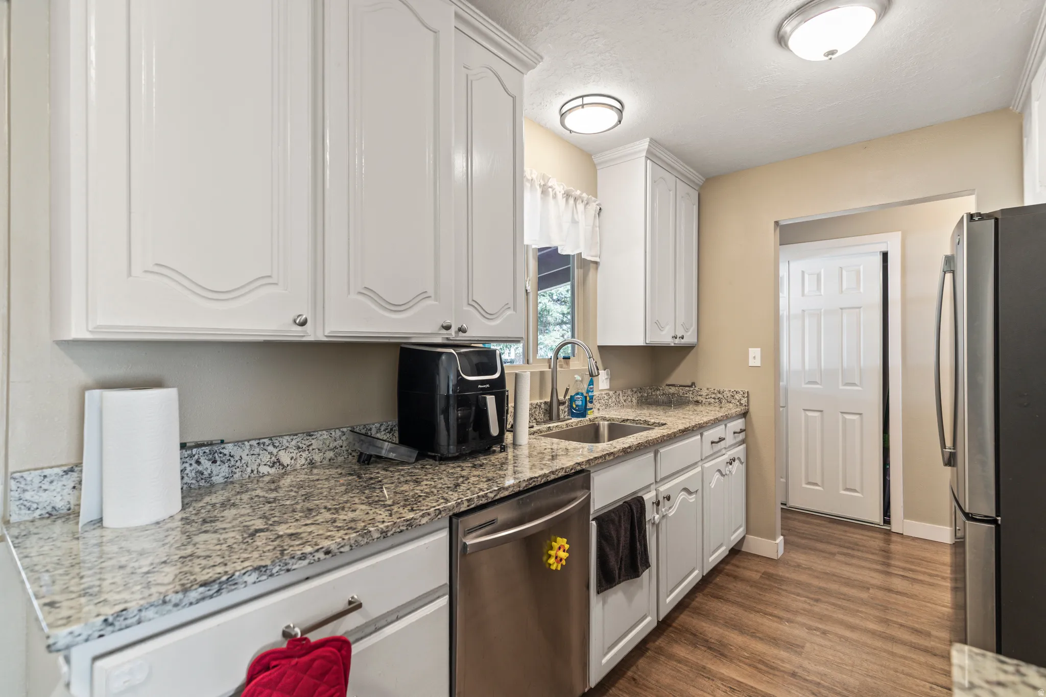 Kitchen featuring white cabinetry, granite countertops, stainless steel dishwasher, double basin sink, and wood-finish flooring
