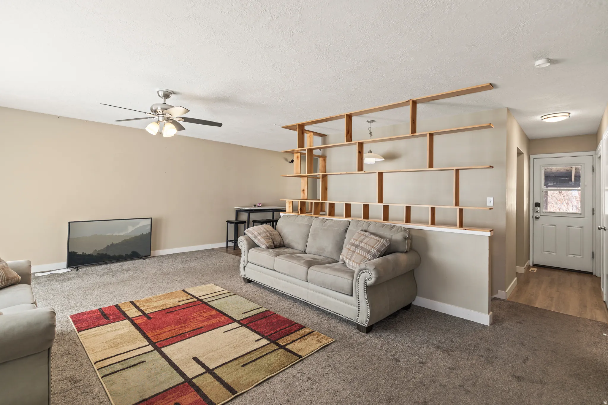 Living area featuring carpet flooring, built-in shelving, a ceiling fan with integrated lighting, and a front entry door with a privacy pane
