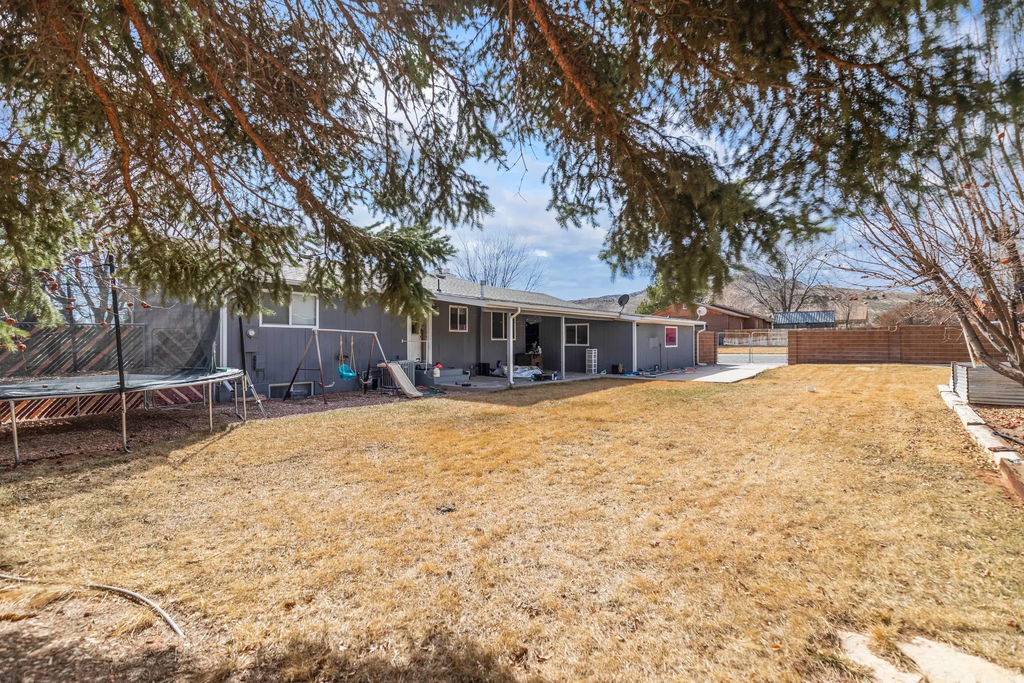 Rear exterior featuring a grey siding facade, multiple windows, a covered patio area, and an expansive lawn