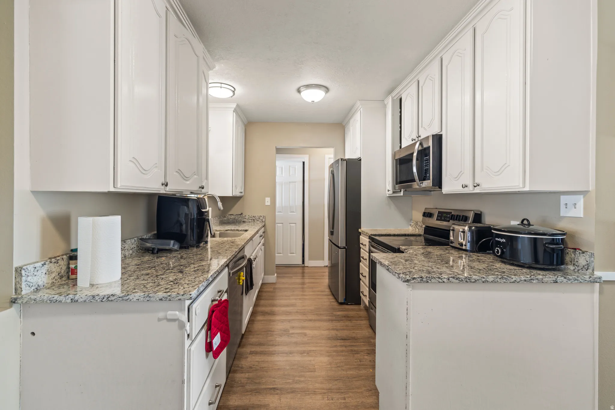 Galley kitchen featuring white cabinetry, light-toned countertops, and wood-finish flooring
