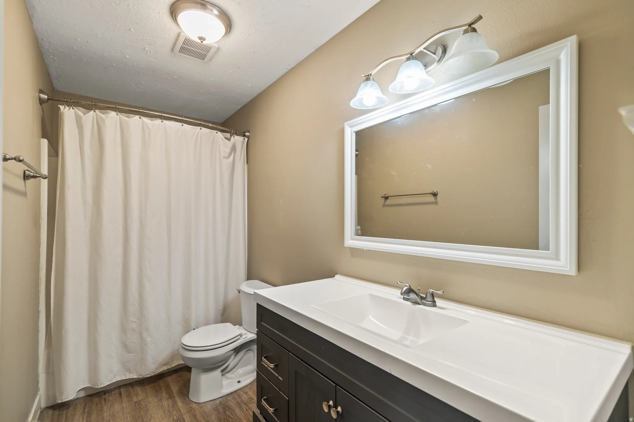 Bathroom featuring a dark wood-finish vanity with a white integrated sink, a large framed mirror, and wood-finish flooring