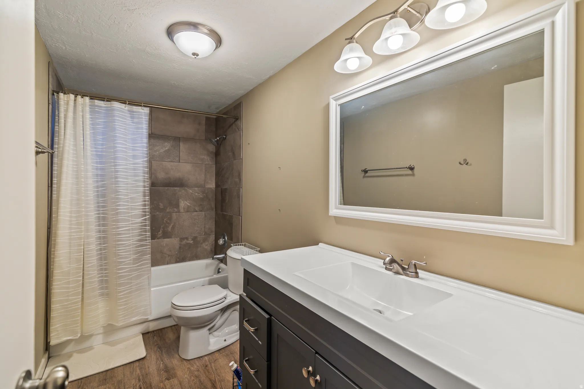 Bathroom featuring a vanity with a white countertop and integrated sink, a rectangular framed mirror, a tub-shower combination with floor-to-ceiling tile surround, and wood-finish flooring