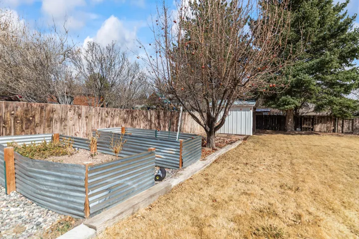 Backyard featuring corrugated metal raised garden beds, a white storage shed, mature trees, and a wooden privacy fence