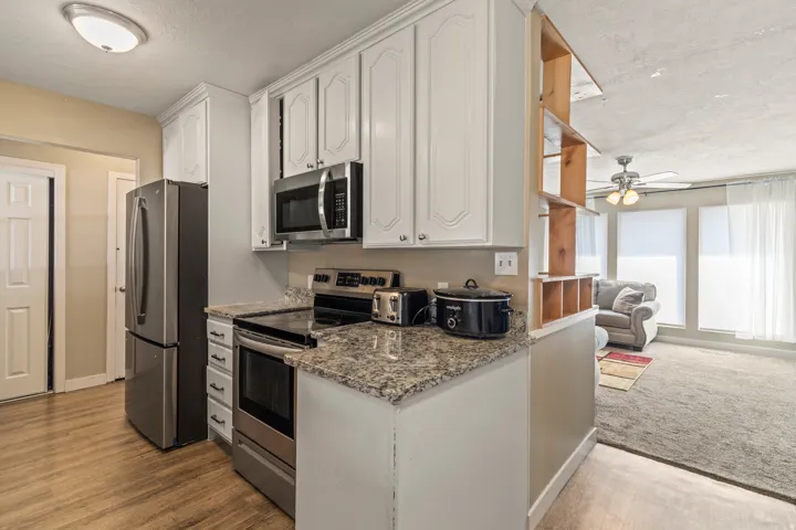 Kitchen featuring white cabinetry, stone-finish countertops, stainless steel appliances, and wood-finish flooring