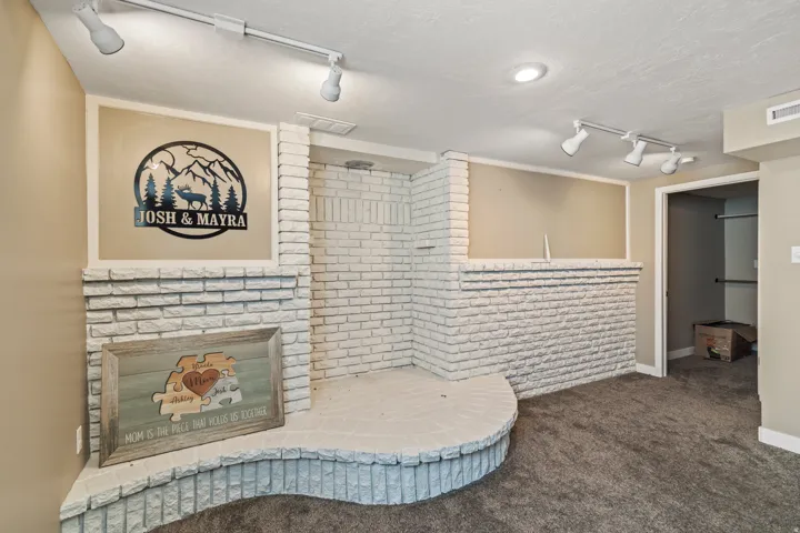 White-painted brick fireplace with a curved hearth, integrated shelving, track lighting, recessed lighting, and carpet flooring