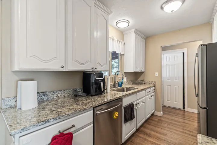 Kitchen featuring white cabinetry, granite countertops, stainless steel dishwasher, double basin sink, and wood-finish flooring