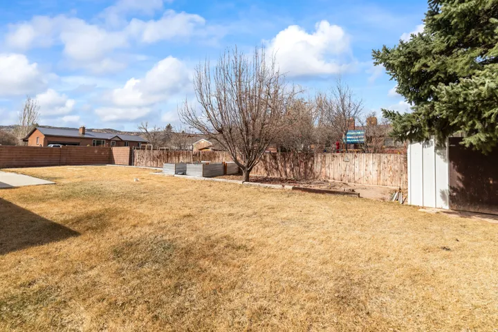 Spacious backyard featuring a concrete patio, mature trees, wood fence, brick privacy wall, and a storage shed