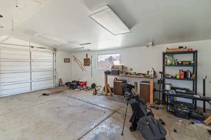 Spacious garage featuring a roll-up door, concrete flooring, overhead fluorescent lighting, and a single window