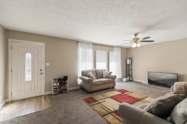 Living area featuring neutral wall tones, textured ceiling, and a ceiling fan with integrated lighting