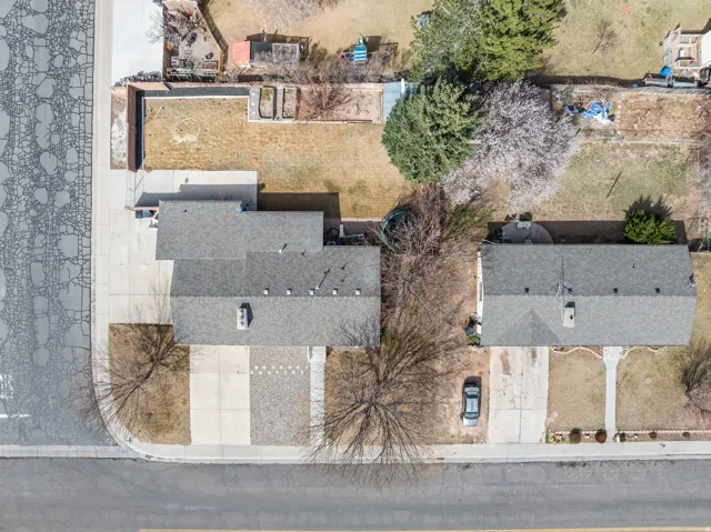 Aerial perspective of two residential properties featuring dark gray shingle roofs, paved driveways, and front yard landscaping