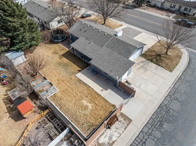 Aerial perspective of a property featuring an L-shaped residence with a two-car garage, an elongated driveway, and a partially covered patio