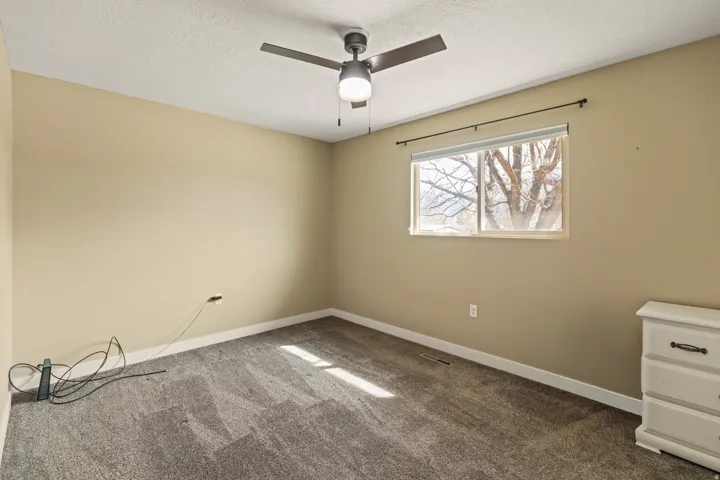 Spacious room featuring gray textured carpeting, neutral wall color, and a modern ceiling fan with integrated lighting
