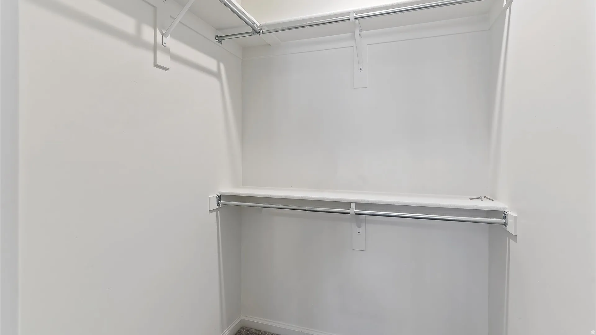 Built-in closet system featuring multiple shelves and hanging rods, white painted walls, and gray carpeting