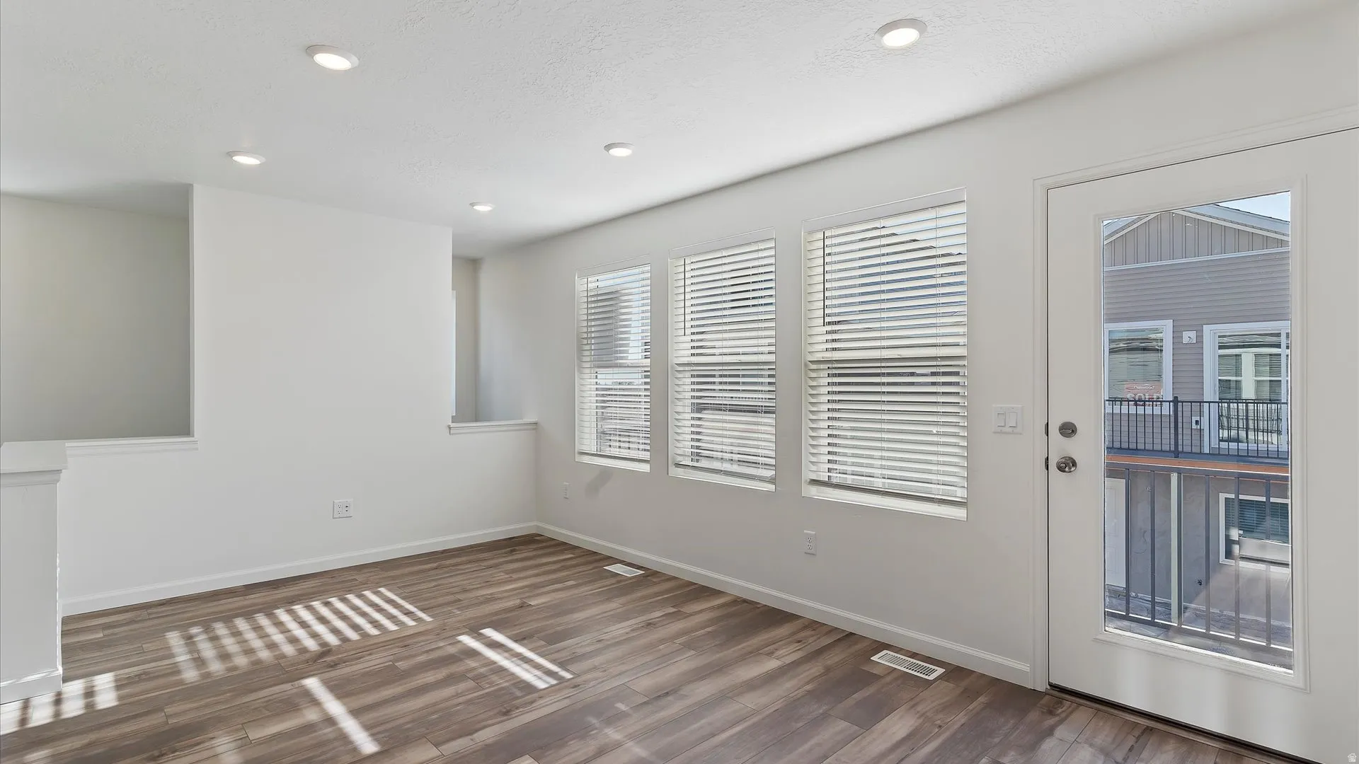 Bright interior space featuring wood-finish flooring, recessed lighting, multiple windows with blinds, and a glass-paneled door