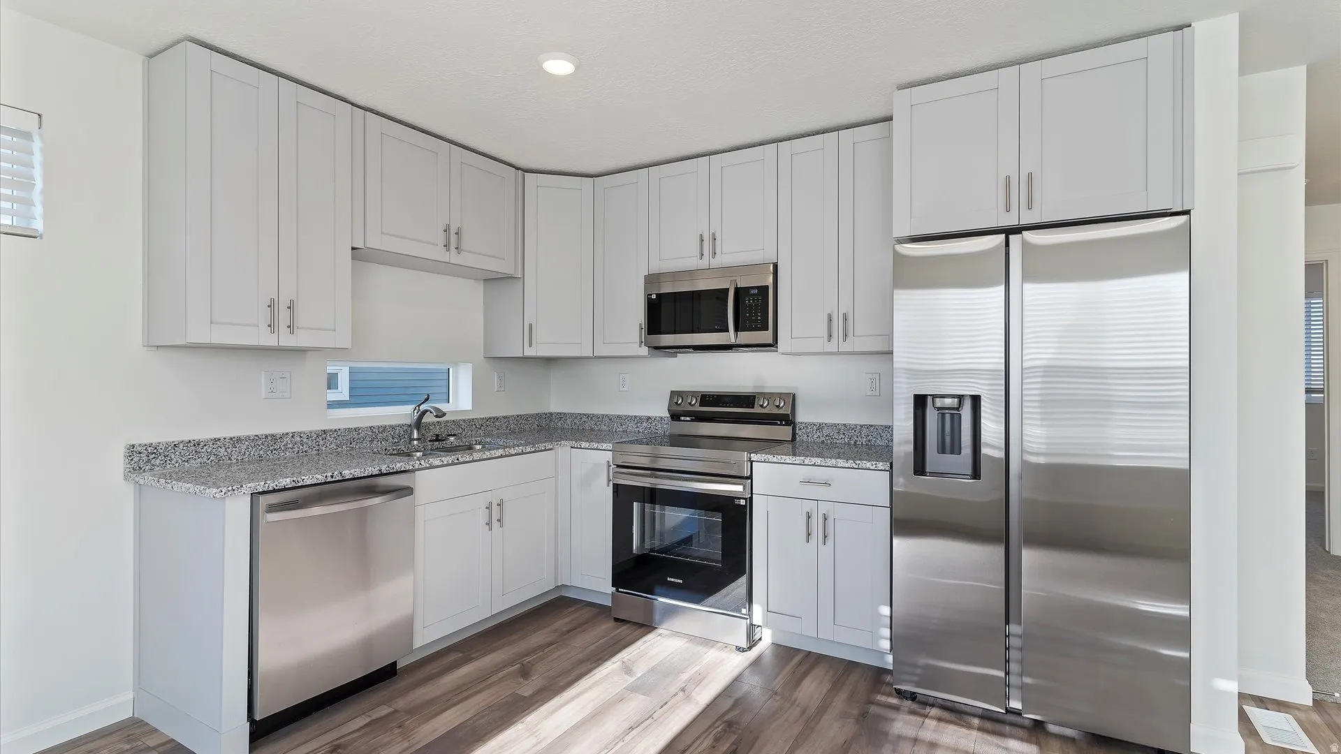 Modern kitchen featuring light gray shaker-style cabinetry, stainless steel appliances, and speckled countertops
