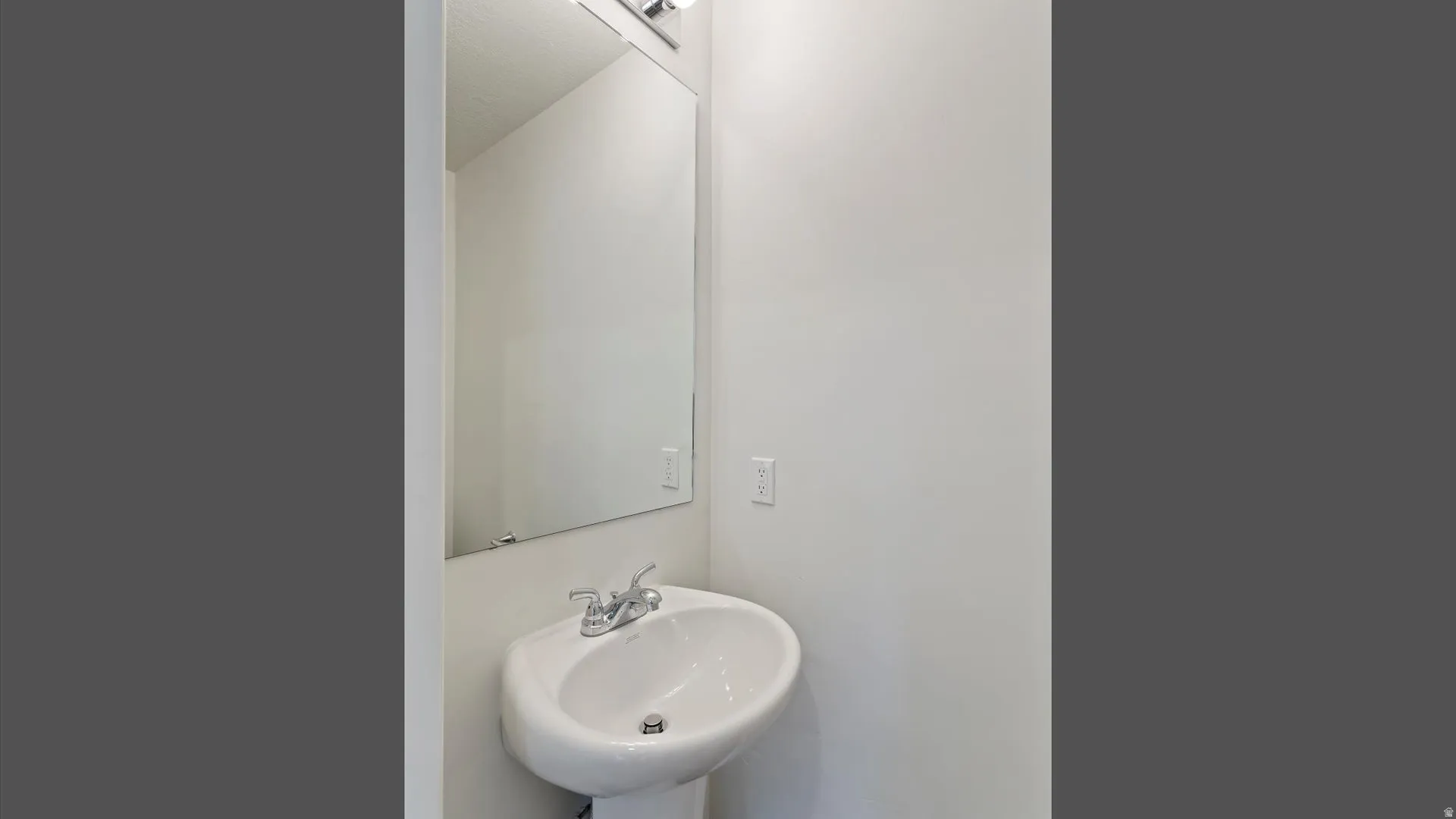 Pedestal sink with chrome faucet, complemented by a large wall-mounted mirror