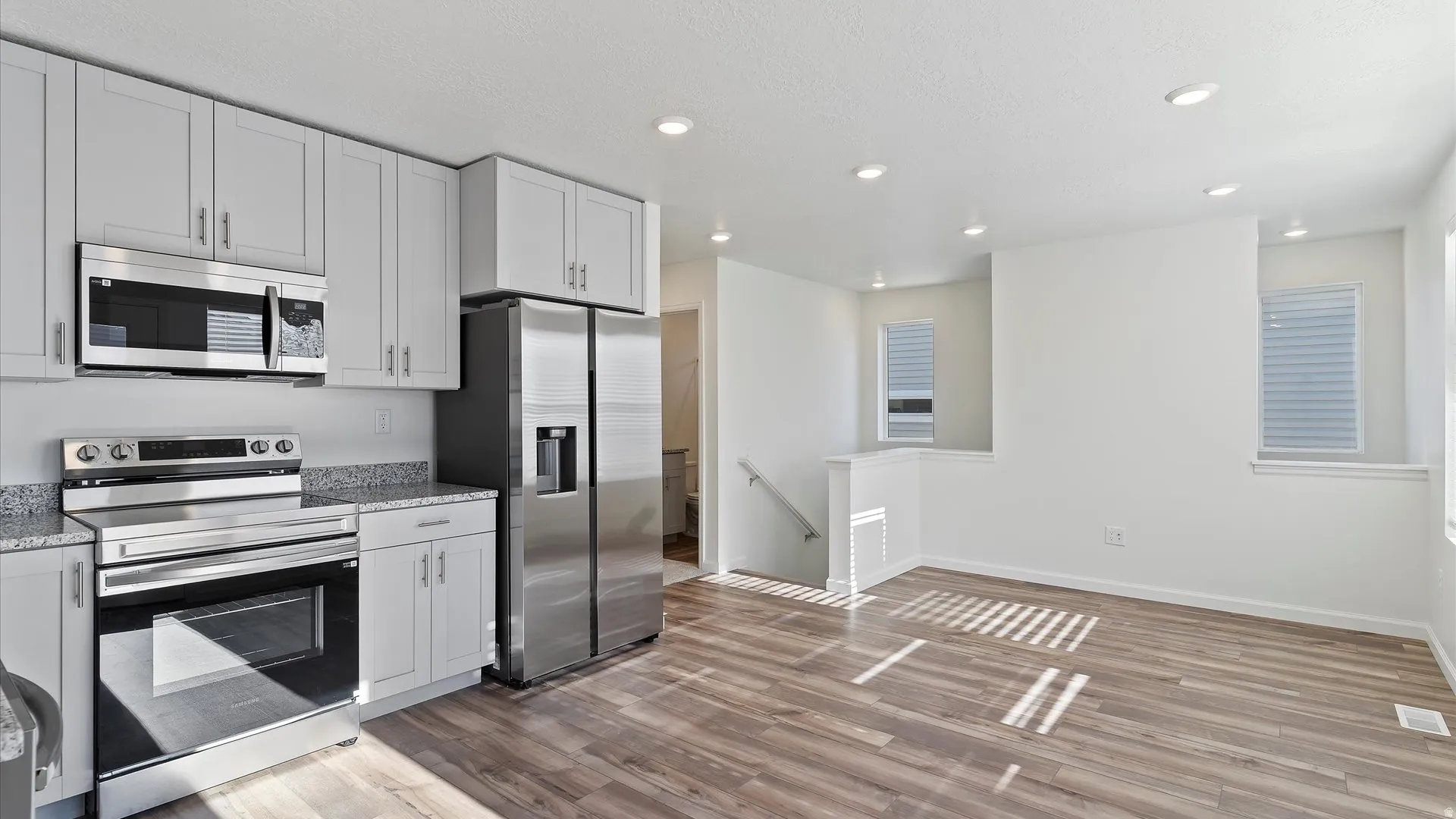 Modern kitchen featuring light gray cabinetry, stainless steel appliances, speckled countertops, wood-finish flooring, and recessed lighting