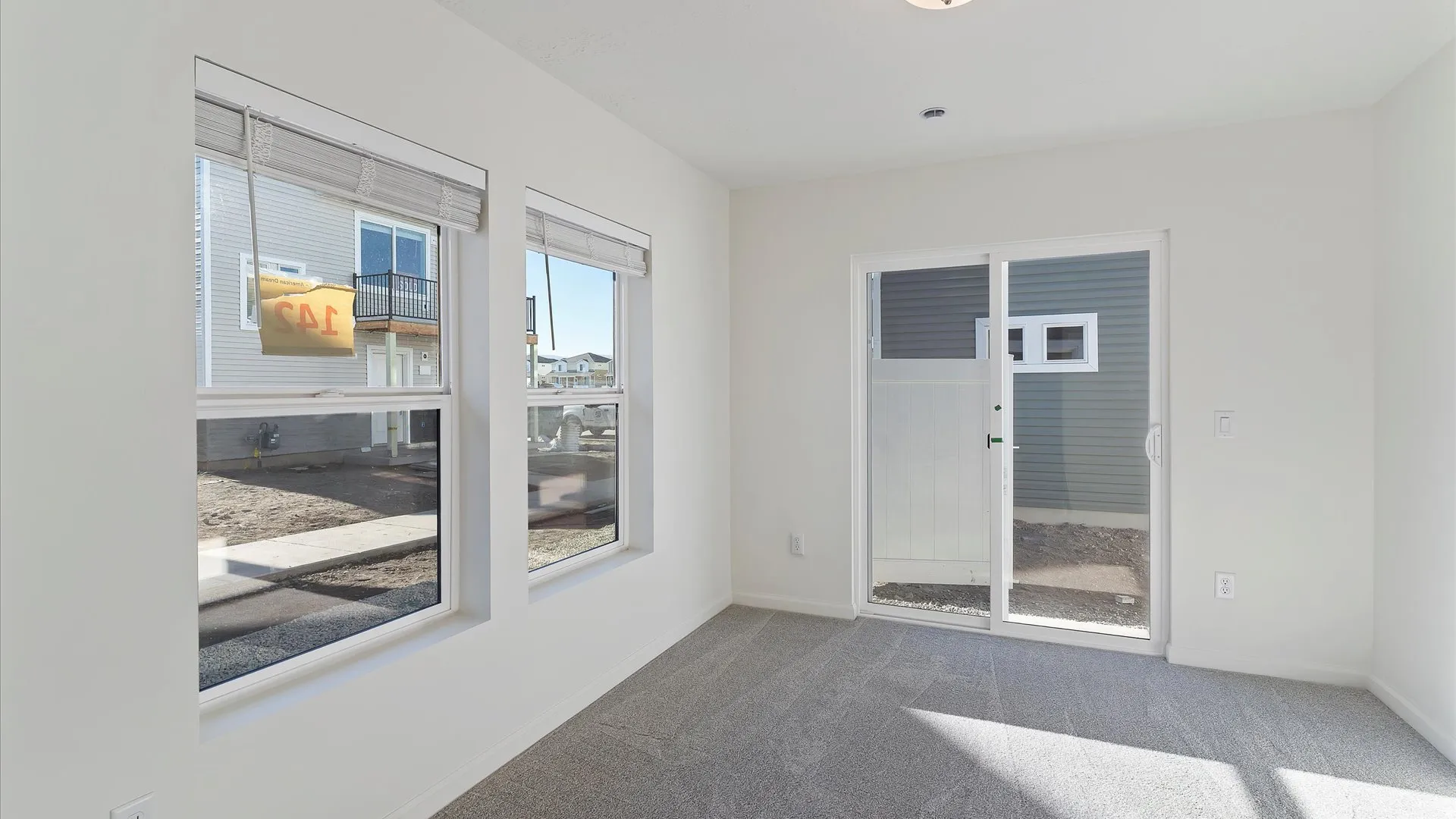 Bright interior space featuring light gray carpet, white painted walls, two large windows with blinds, and a sliding glass door
