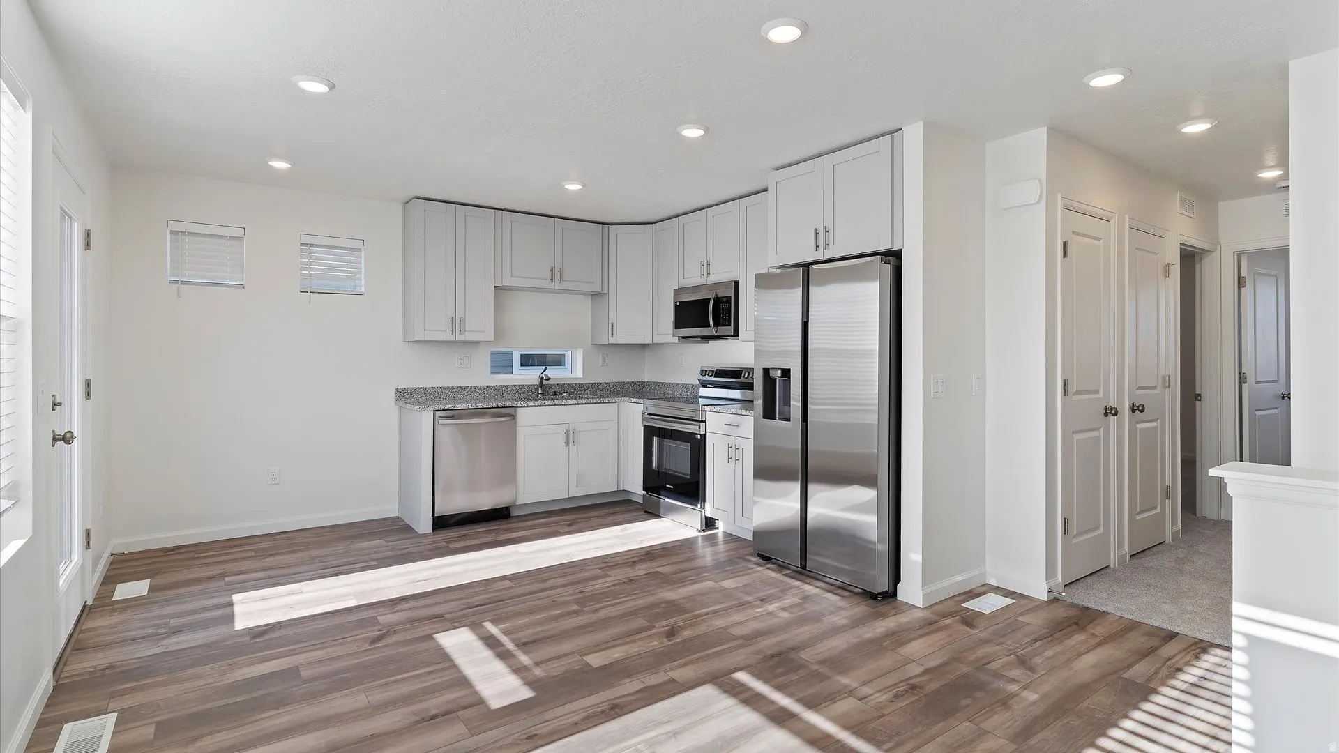 Contemporary kitchen featuring light-toned cabinetry, stainless steel appliances, speckled countertops, wood-finish flooring, and recessed lighting