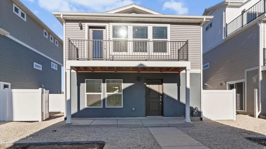 Two-story exterior featuring a second-level balcony with black railing, light gray siding, and a dark gray stucco-finish lower level