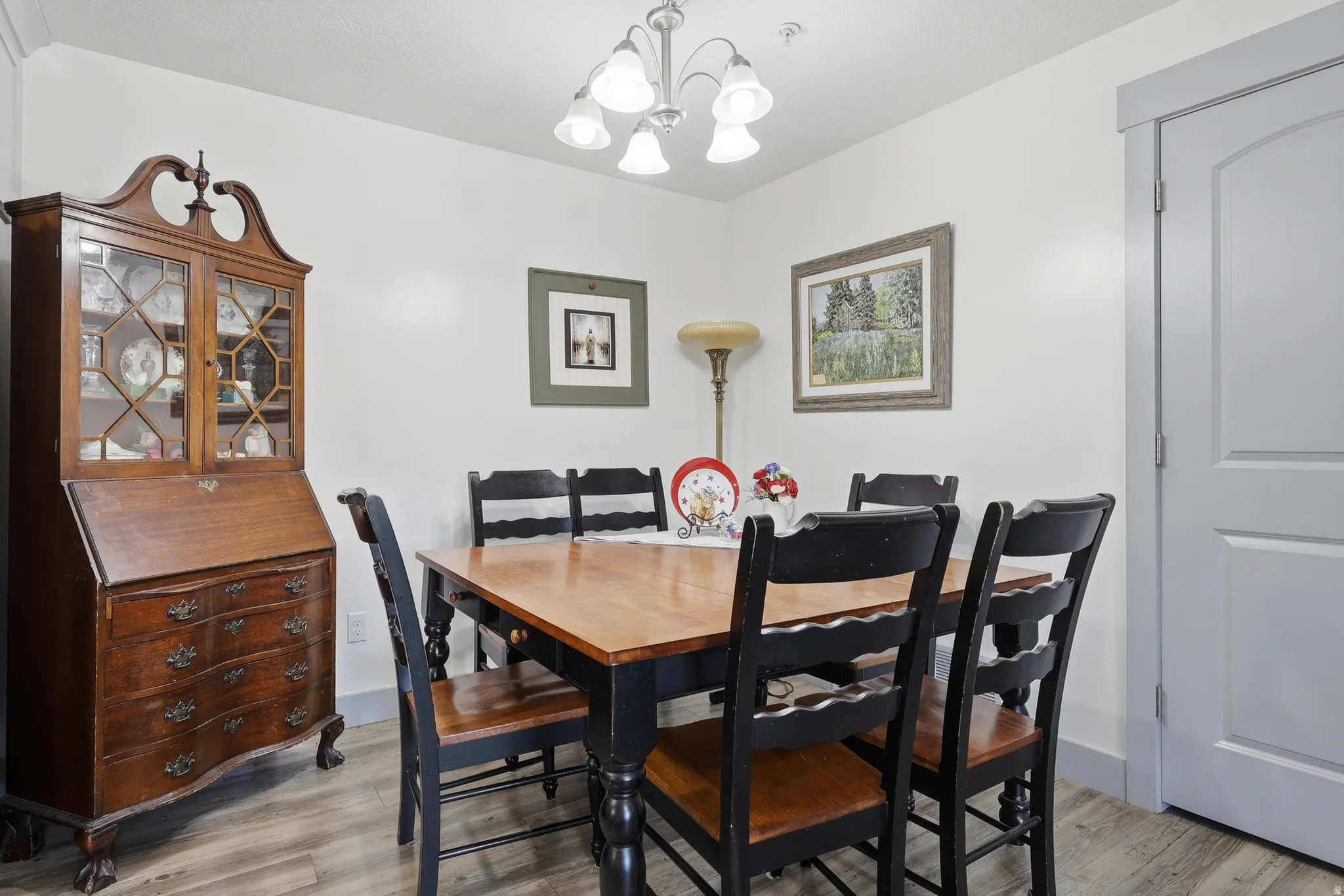 Dining area featuring wood-finish flooring, a contemporary ceiling fixture, white walls, and a gray paneled door