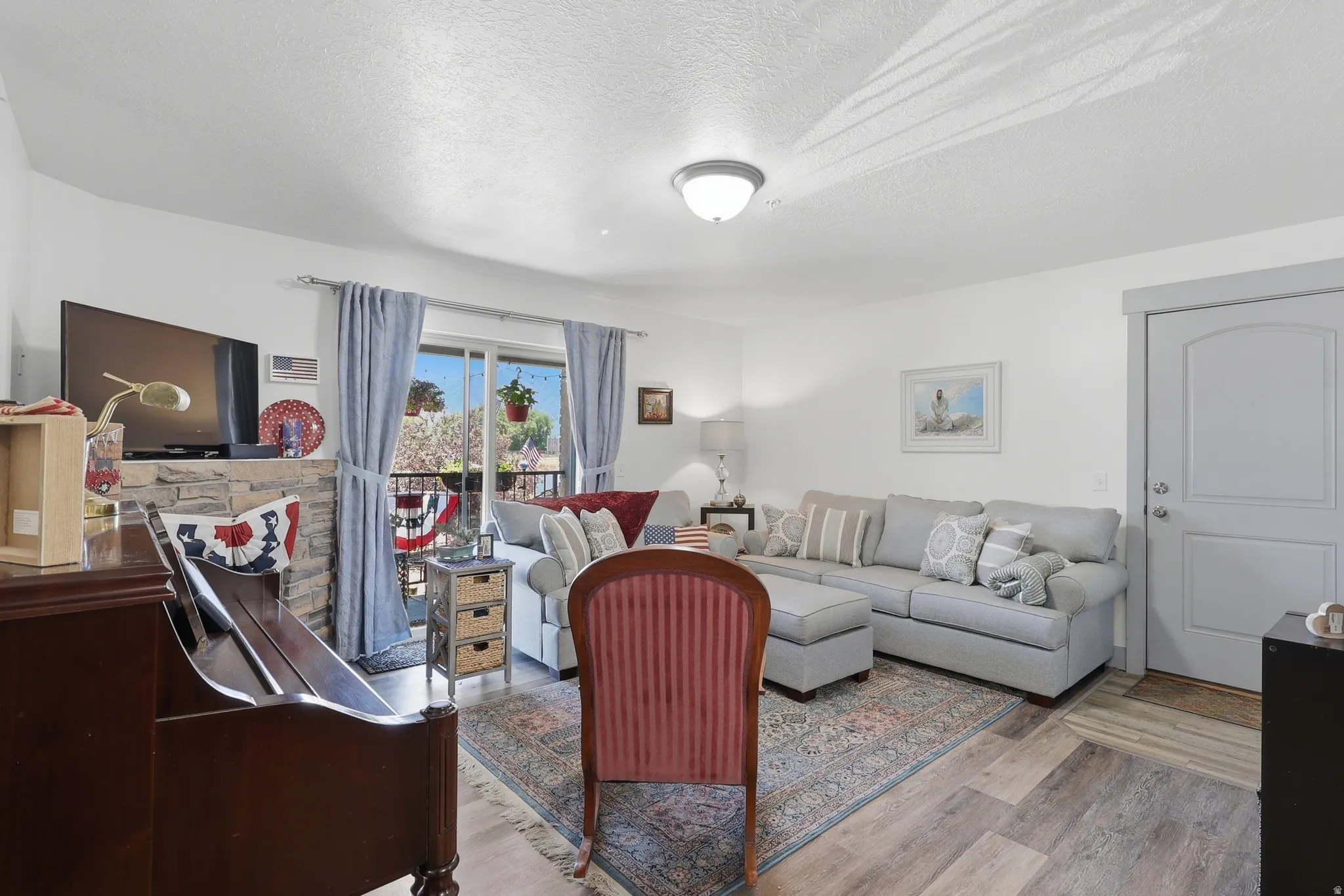 Living area featuring wood-finish flooring, a stone-clad fireplace surround, white walls, and a sliding glass door