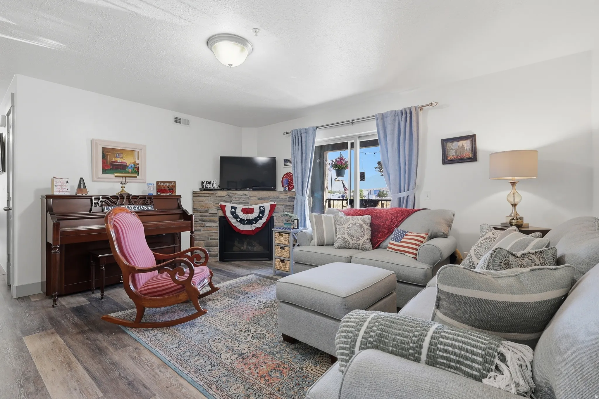 Spacious living area featuring wood-finish flooring, a stone-clad fireplace with mantel, and a sliding glass door
