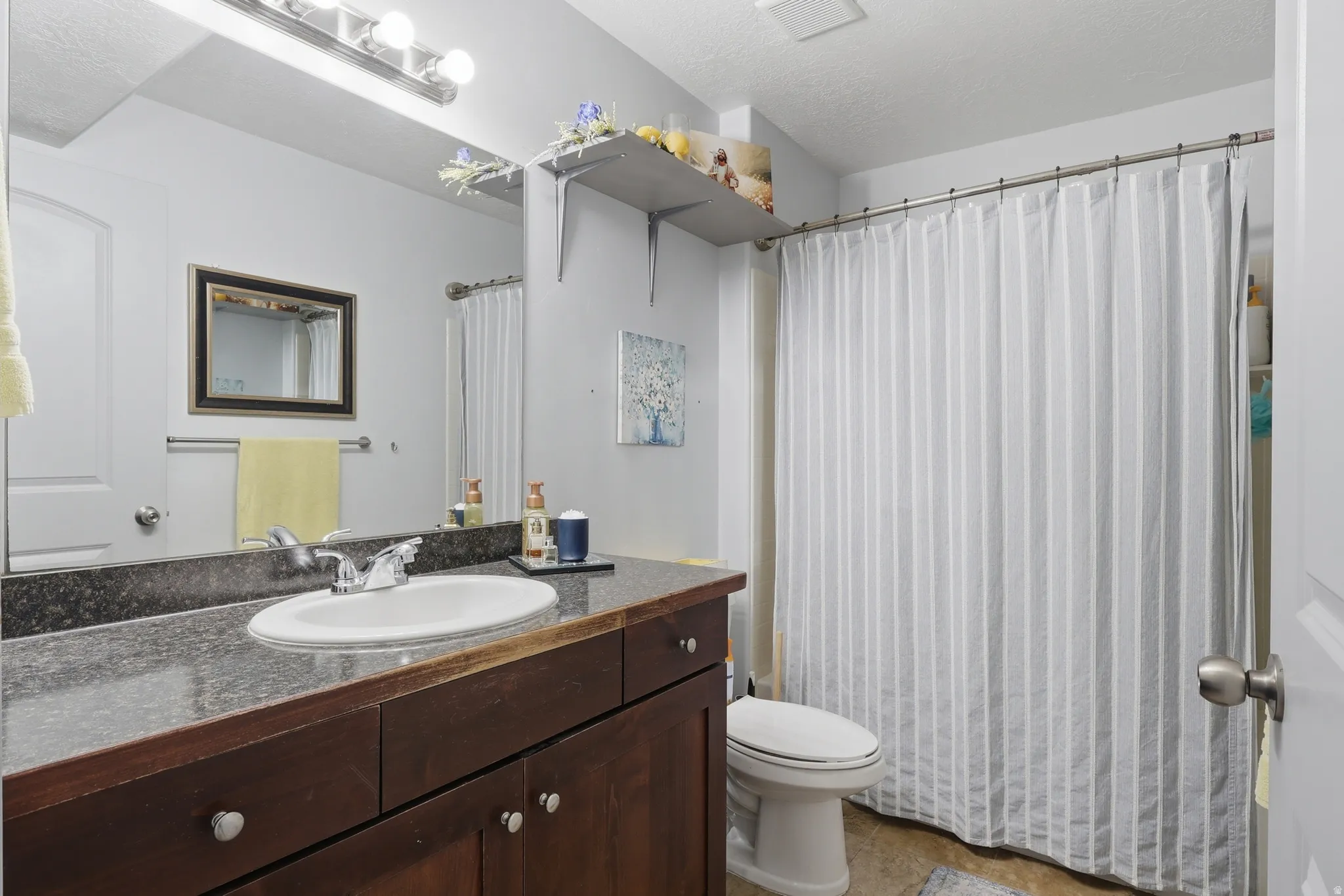 Bathroom featuring a wood-finish vanity with a dark countertop, an oval undermount sink, and a chrome faucet