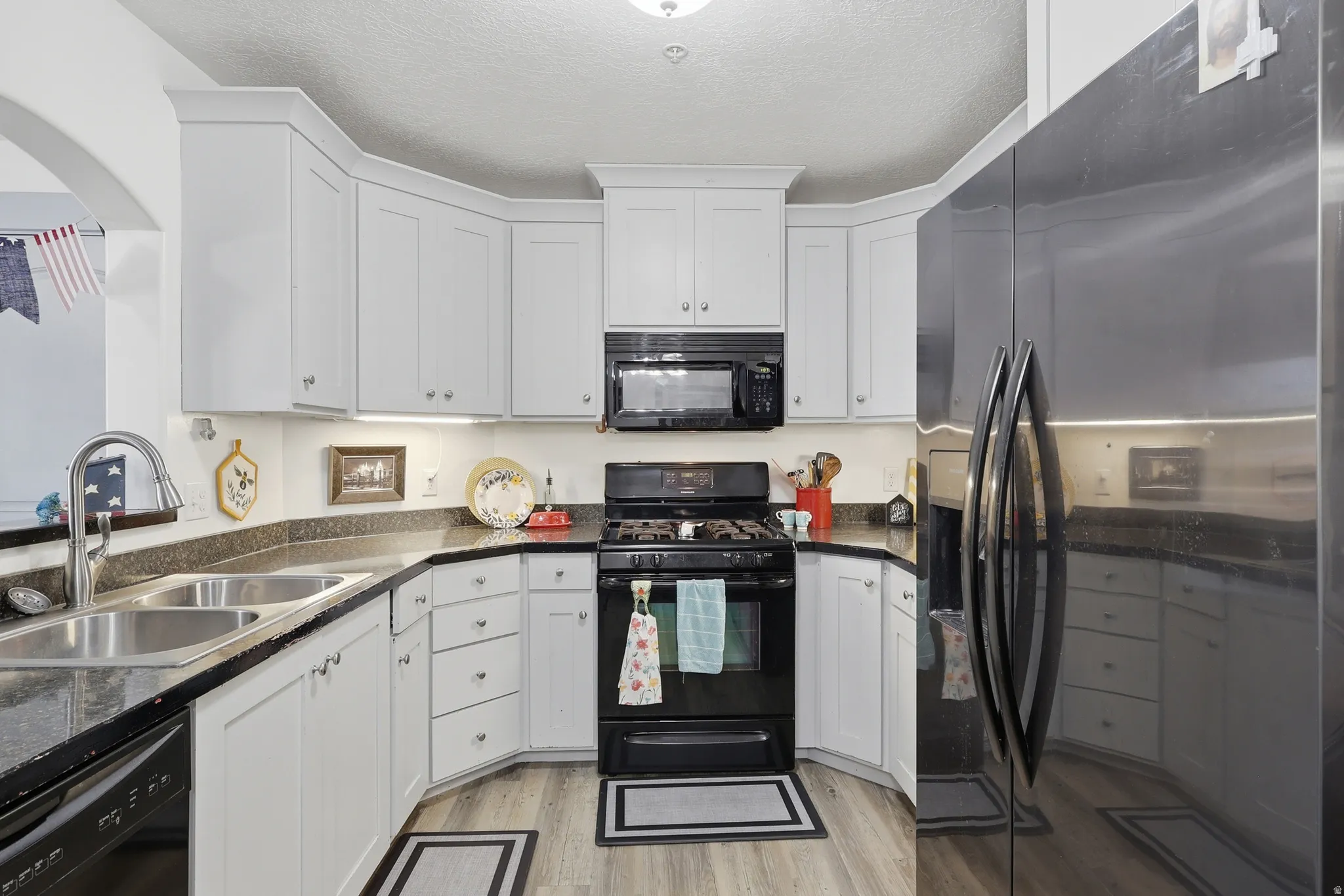 Modern kitchen featuring white cabinetry, dark countertops, a black gas range, and a double-basin stainless steel sink