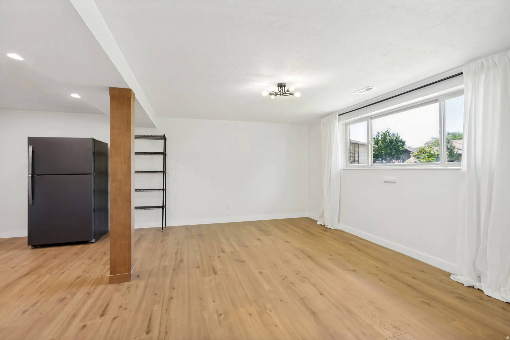 Spacious room featuring wood-finish flooring, a large window with white curtains, and recessed lighting