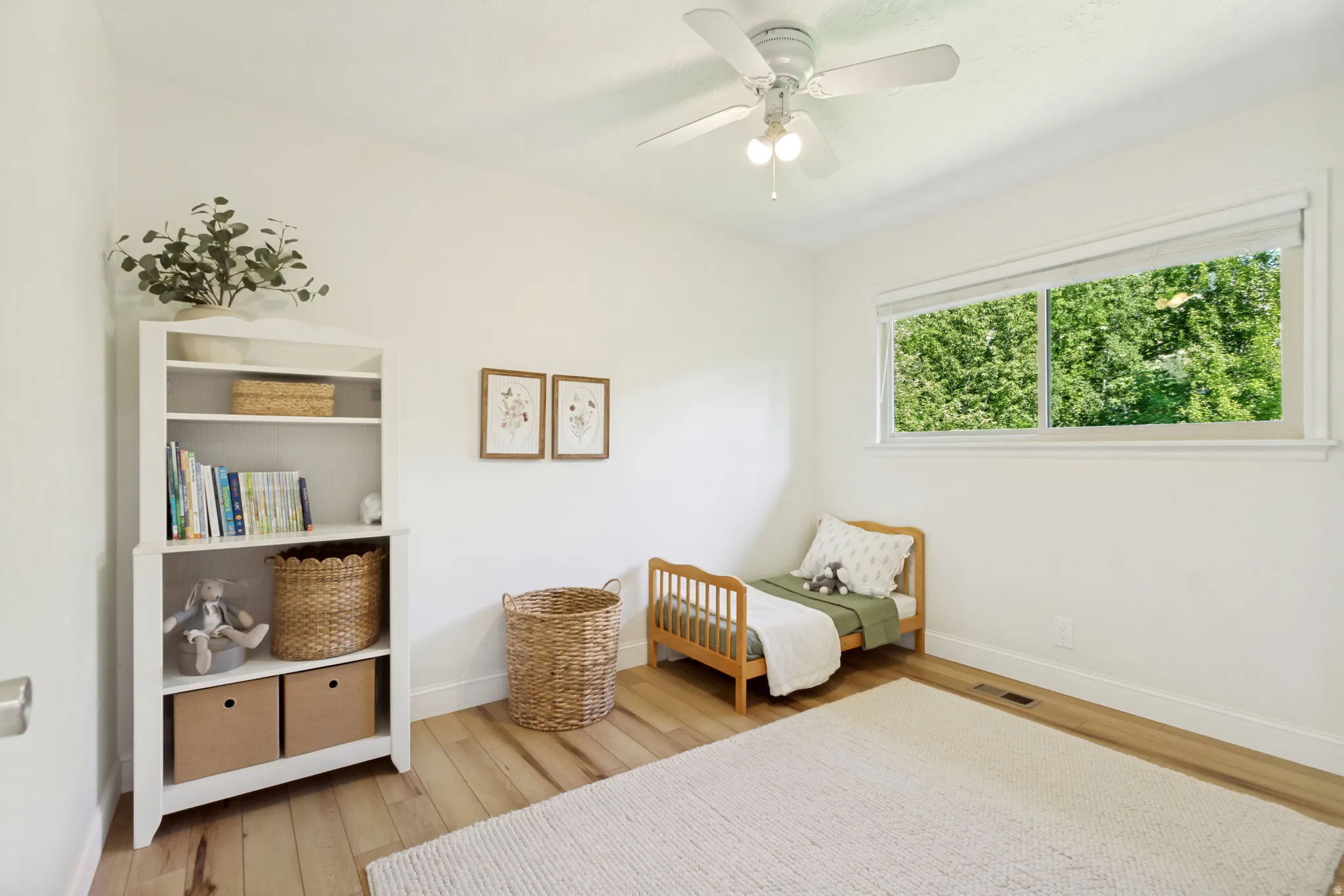 Bright interior space featuring a ceiling fan with light fixture, wood-finish flooring, white baseboards, and a large horizontal window