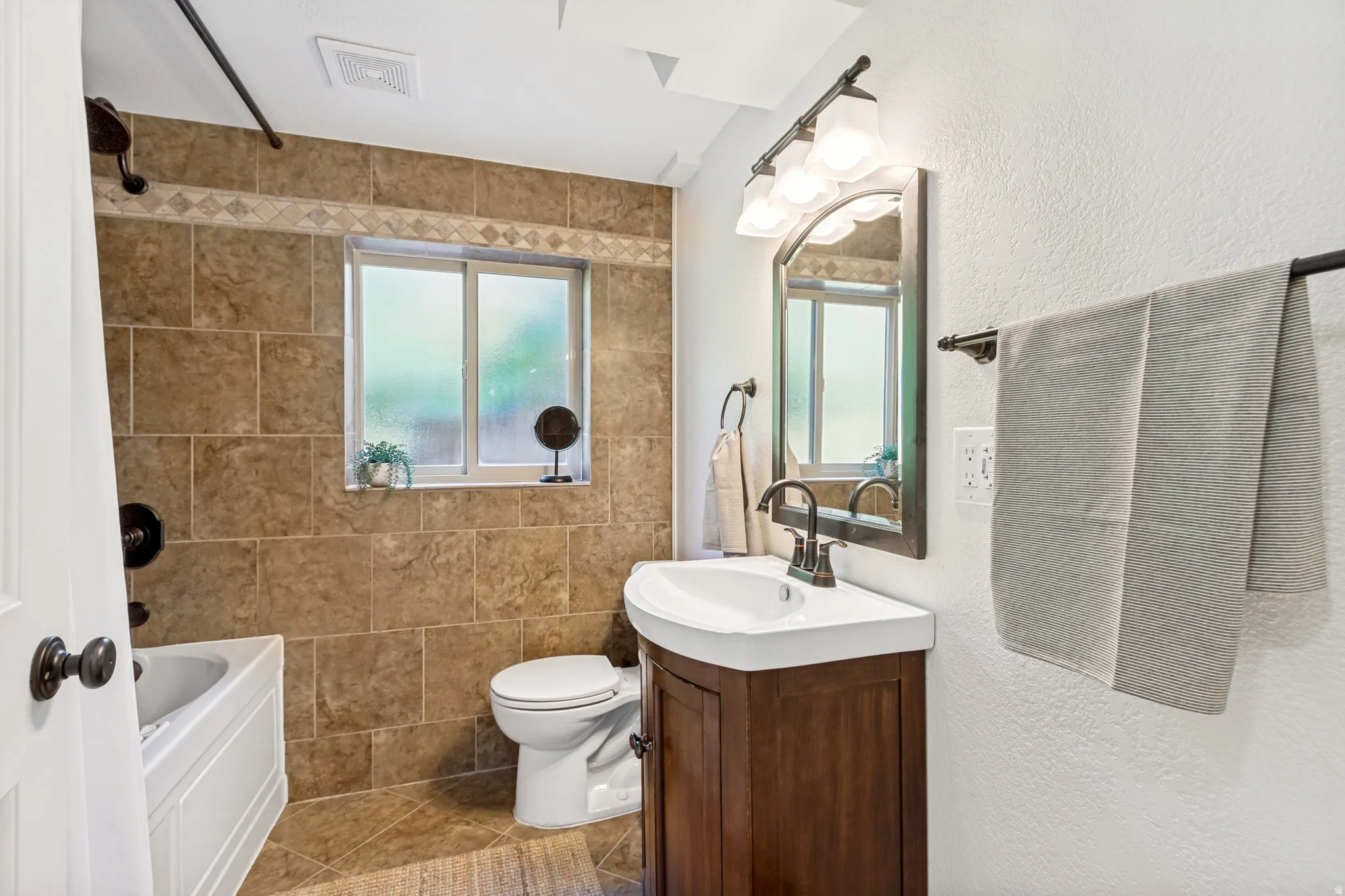 Bathroom featuring a wood-finish vanity with a white countertop, bronze-finish faucet, and coordinating arched mirror