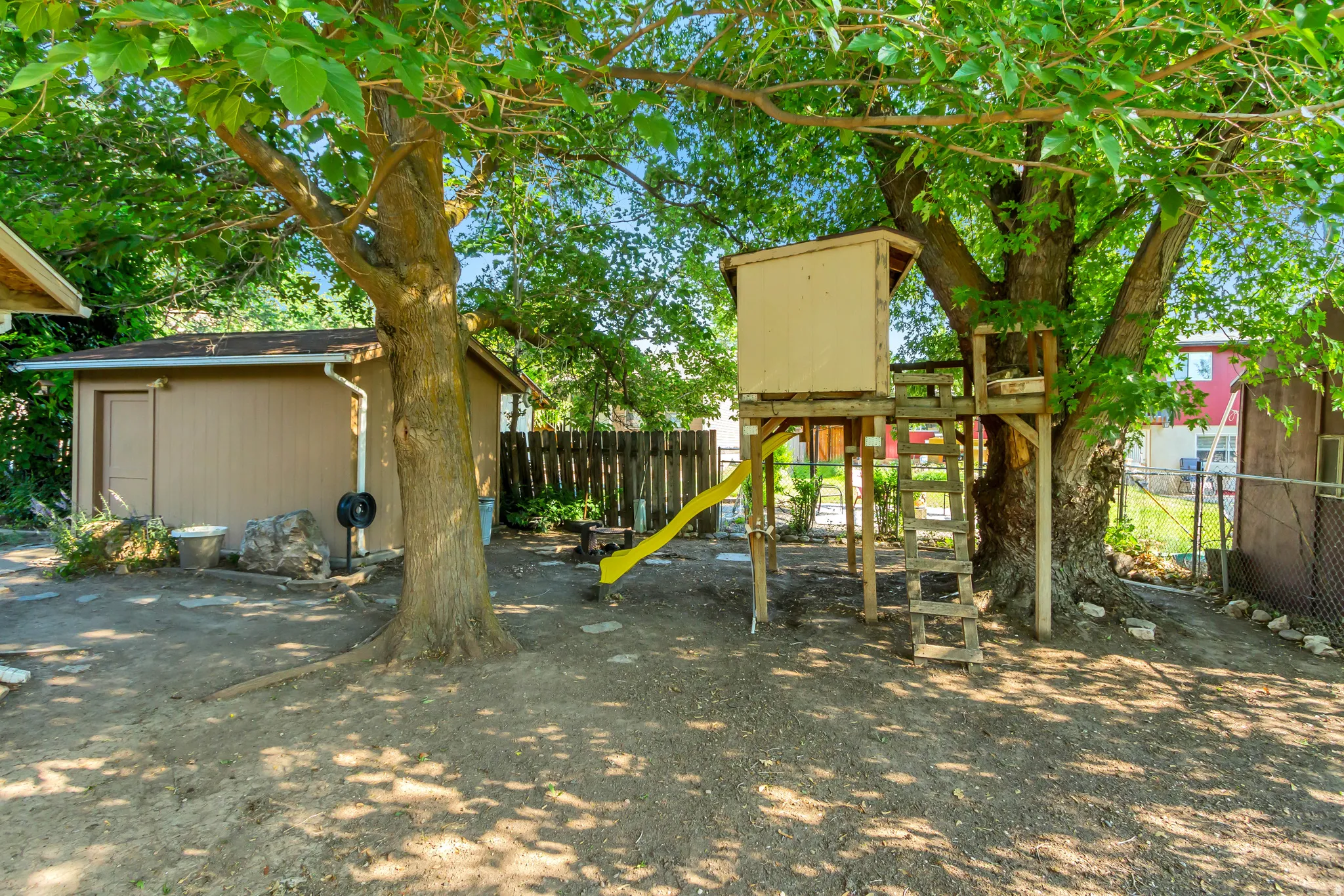 Backyard featuring an established treehouse with a slide, a storage shed, and mature trees providing natural shade