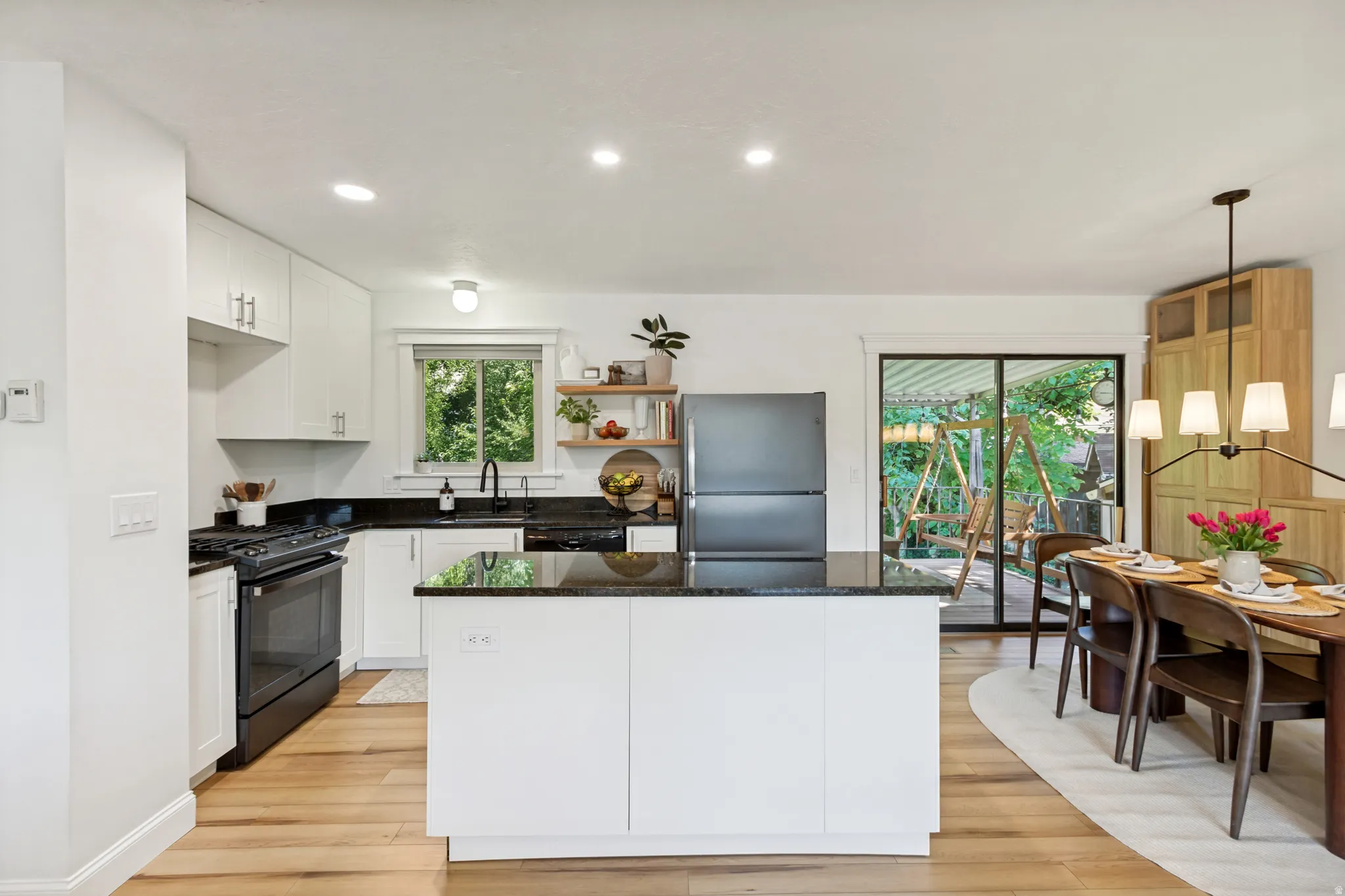 Kitchen featuring white cabinetry, black stone countertops, wood-finish flooring, a central island, and sliding glass doors to the exterior
