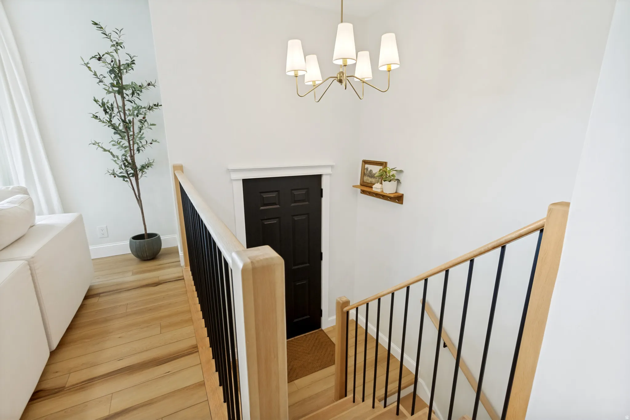 Staircase featuring wood-finish treads and handrails, black metal balusters, and a contemporary chandelier
