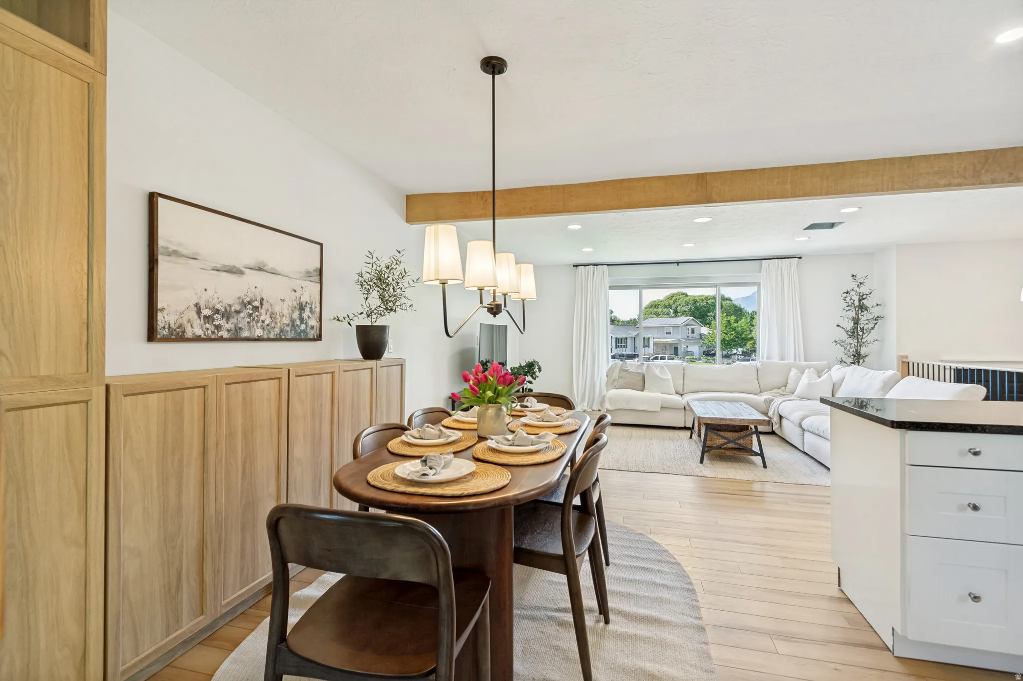 Open-concept living space featuring wood-finish flooring, a contemporary chandelier, built-in cabinetry, and a prominent wood beam accent