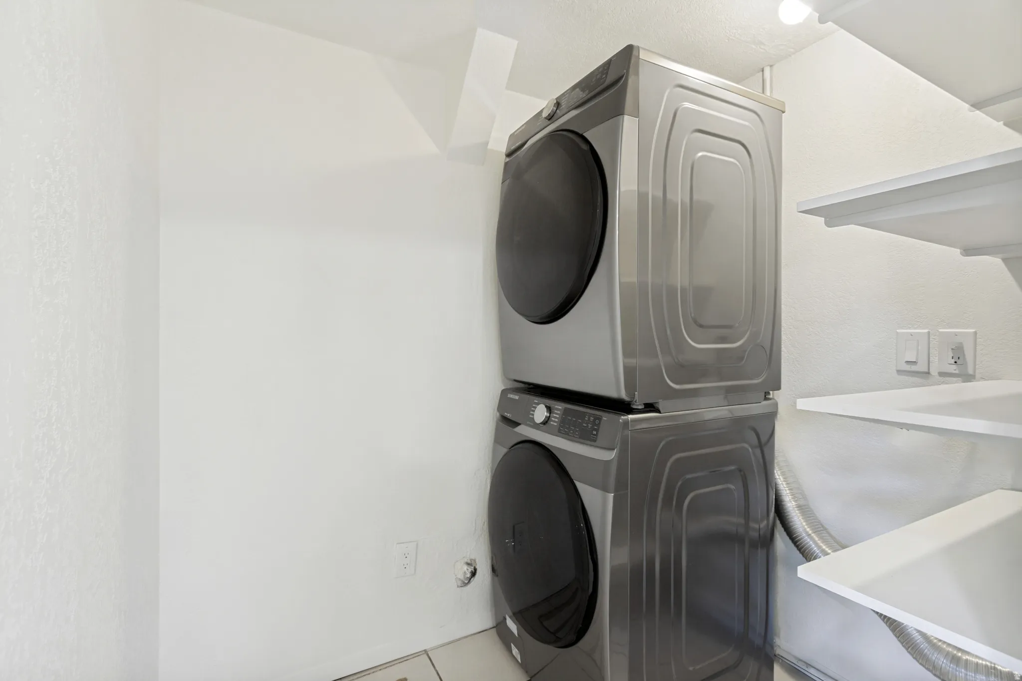 Dedicated laundry space featuring a stacked washer and dryer, white shelving, and tile flooring