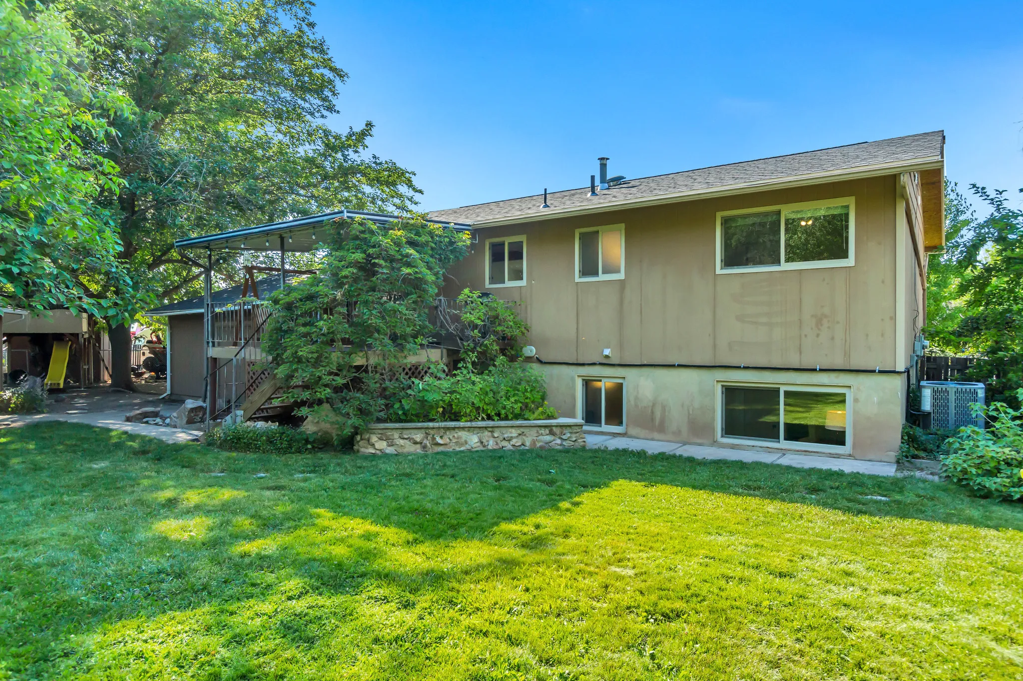 Expansive rear yard featuring a manicured lawn, established trees, and a multi-level deck with a covered portion