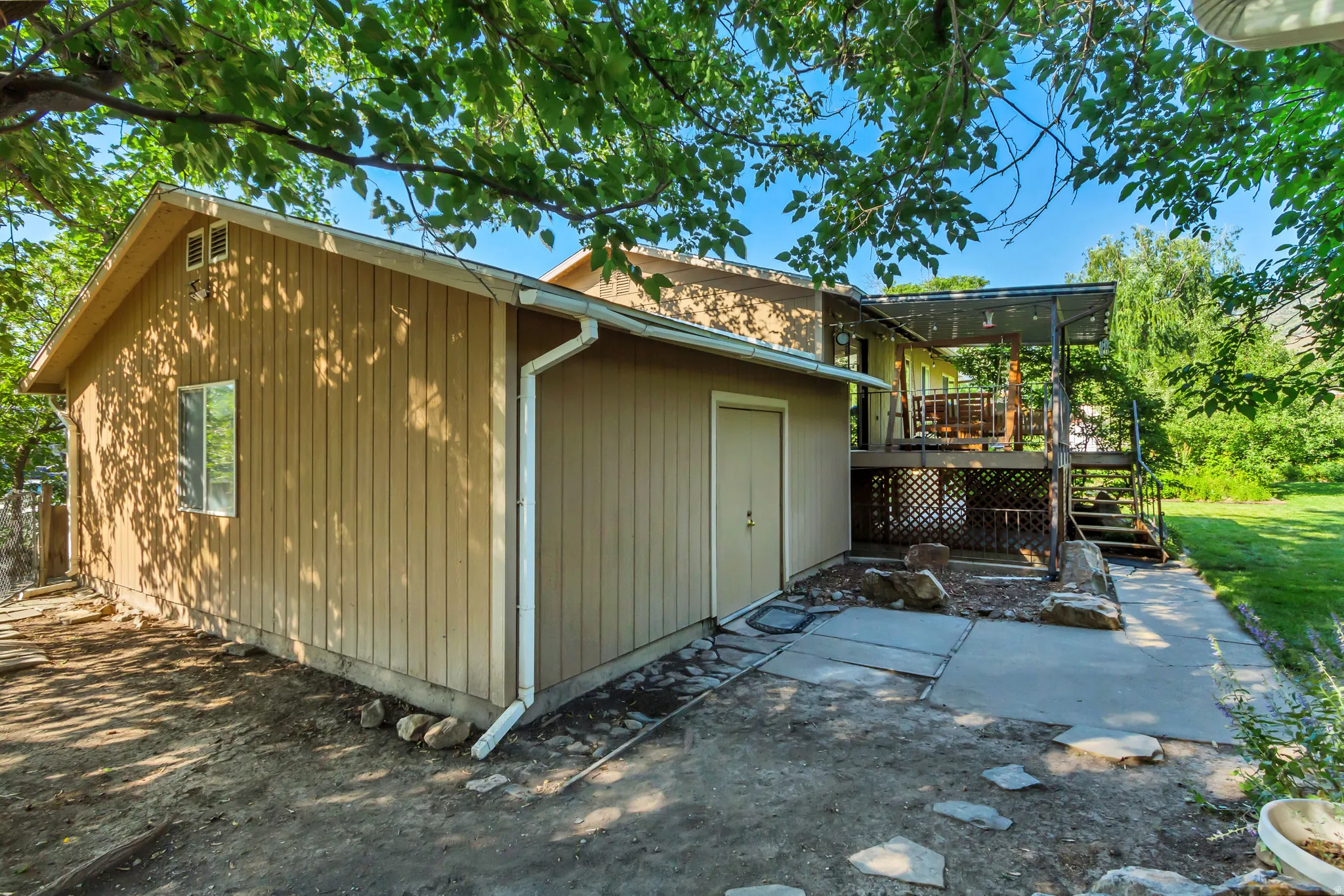 Exterior featuring board-and-batten siding, a covered upper-level deck, concrete patio, and a separate storage room entrance