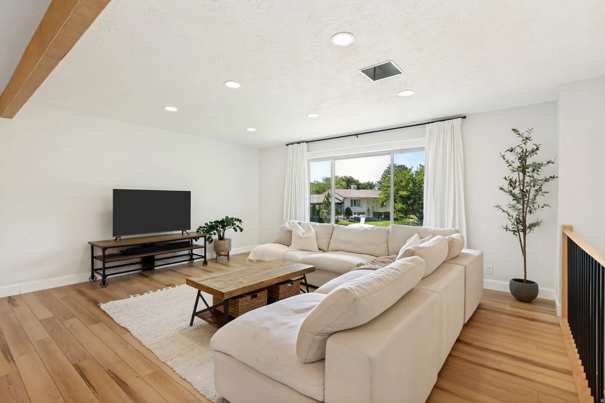Bright living area with wood-finish flooring, recessed lighting, and a large picture window