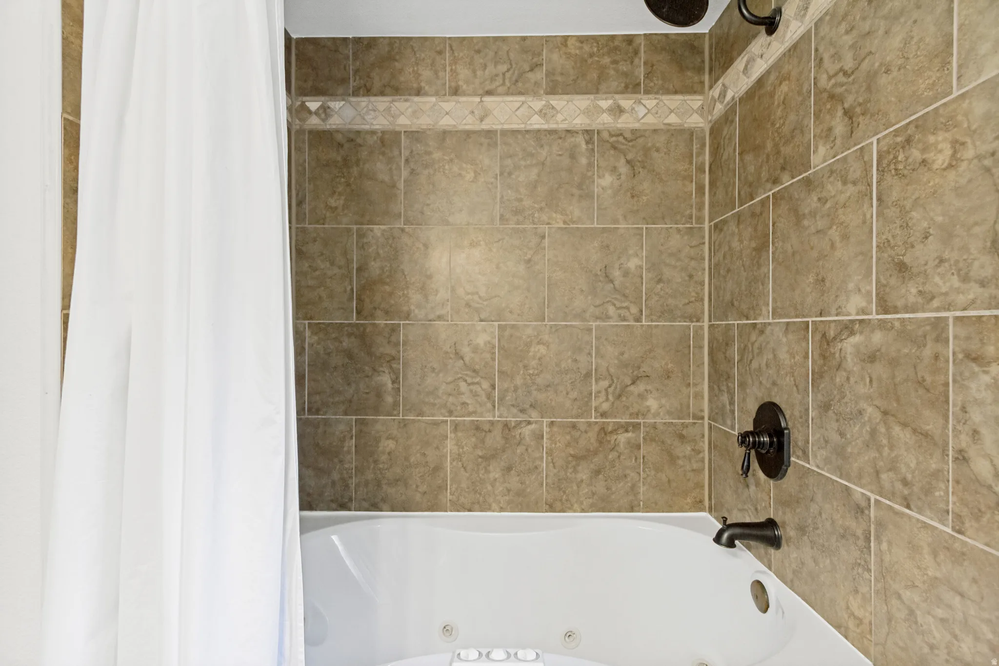 Soaking tub with integrated jets and bronze fixtures, surrounded by large format wall tile