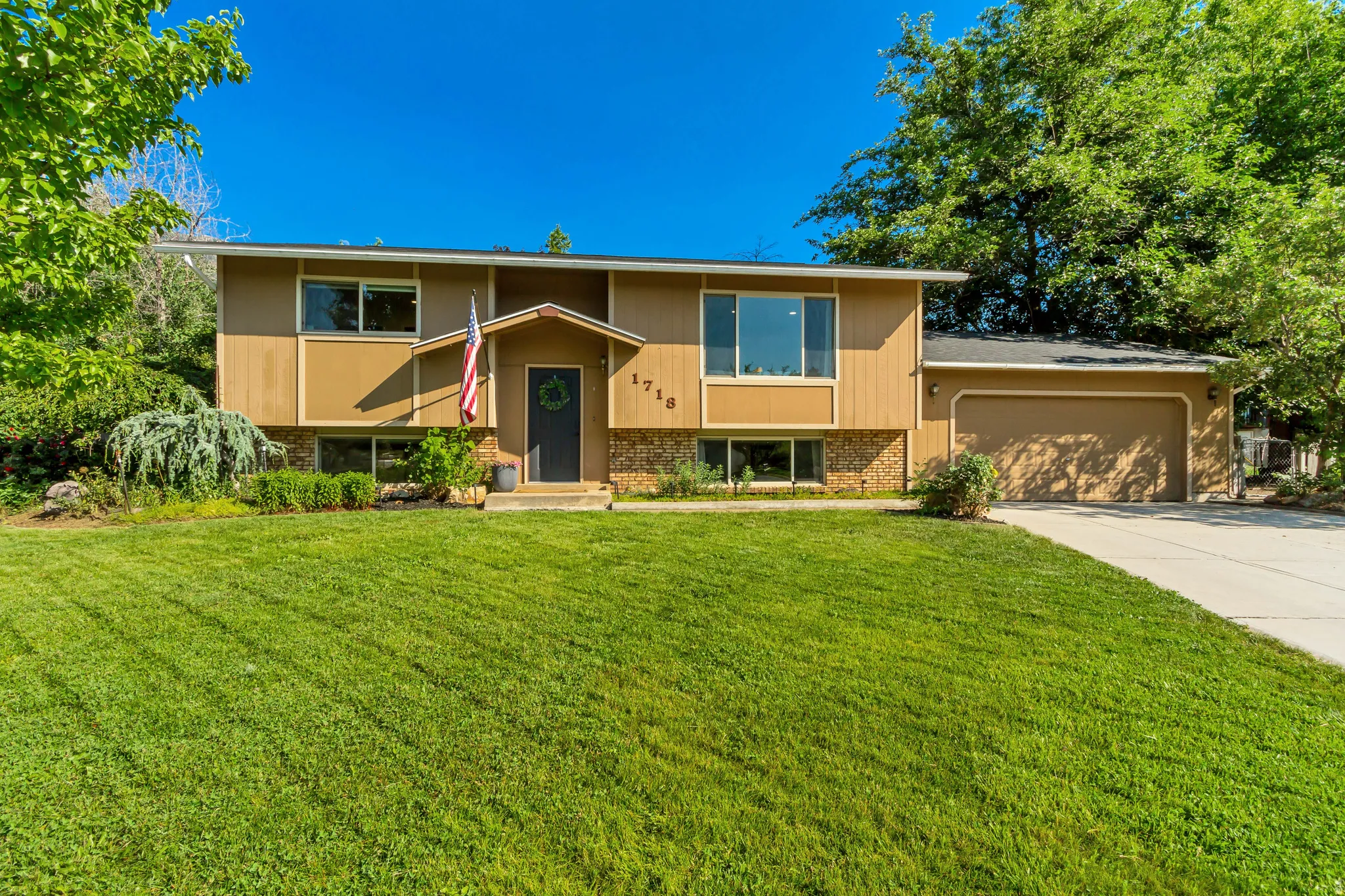 Split-level residence featuring a two-car garage, mature landscaping, and an expansive front lawn