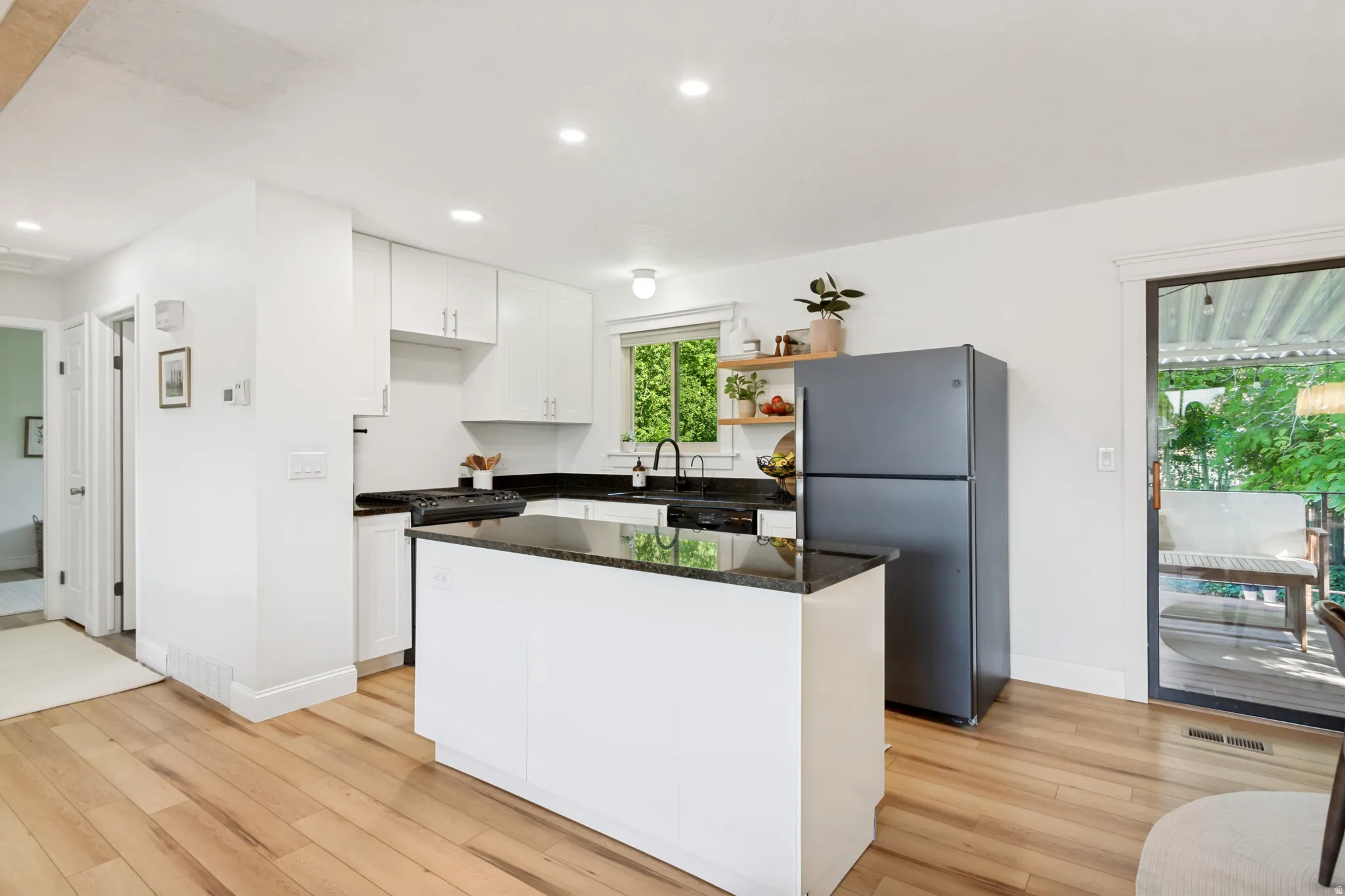 Kitchen featuring white cabinetry, dark stone countertops, wood-finish flooring, a kitchen island, and a sliding glass door leading to an outdoor space