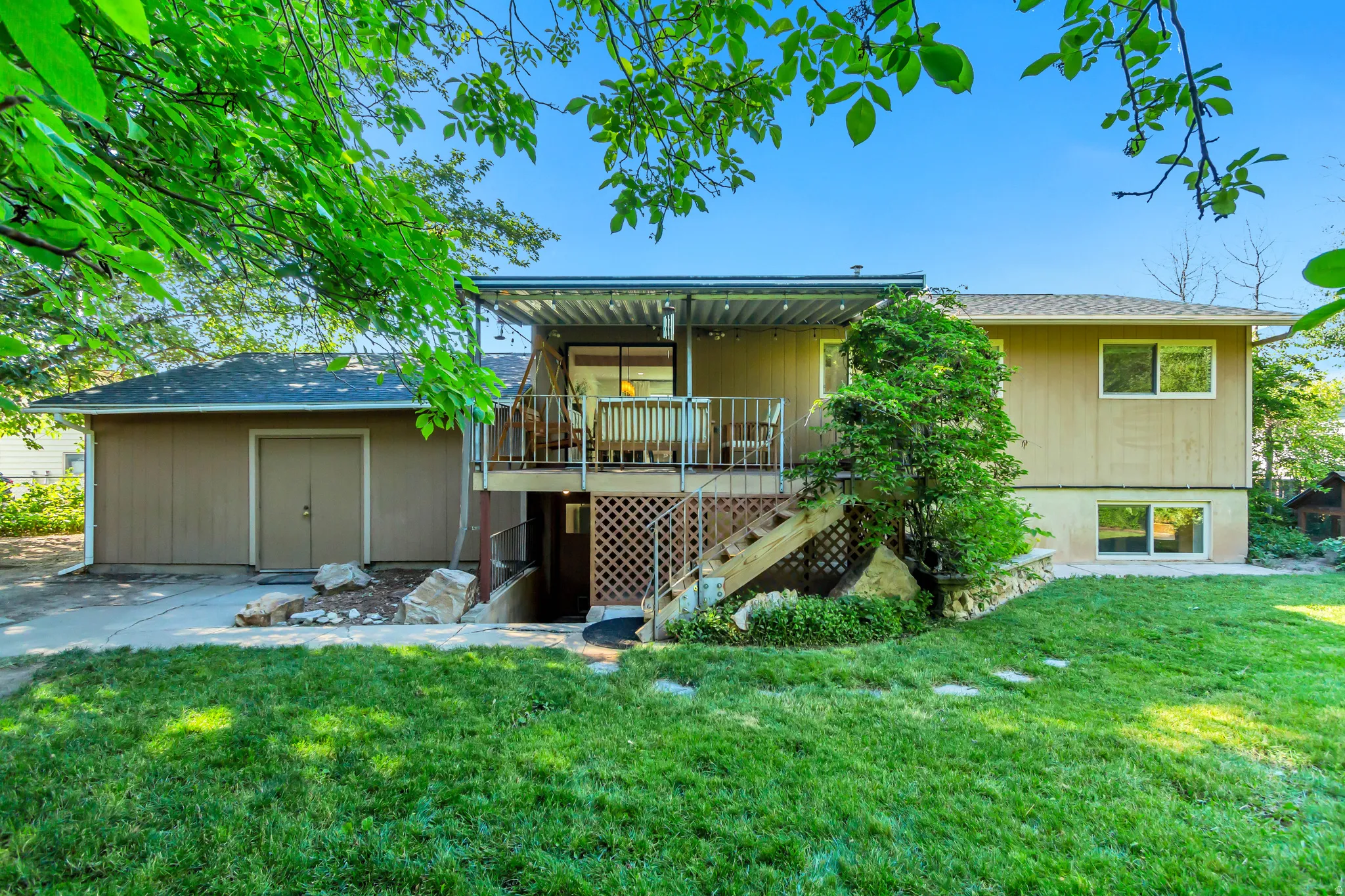 Expansive backyard featuring a manicured lawn, established landscaping, a multi-level deck with a covered patio, and a separate storage structure