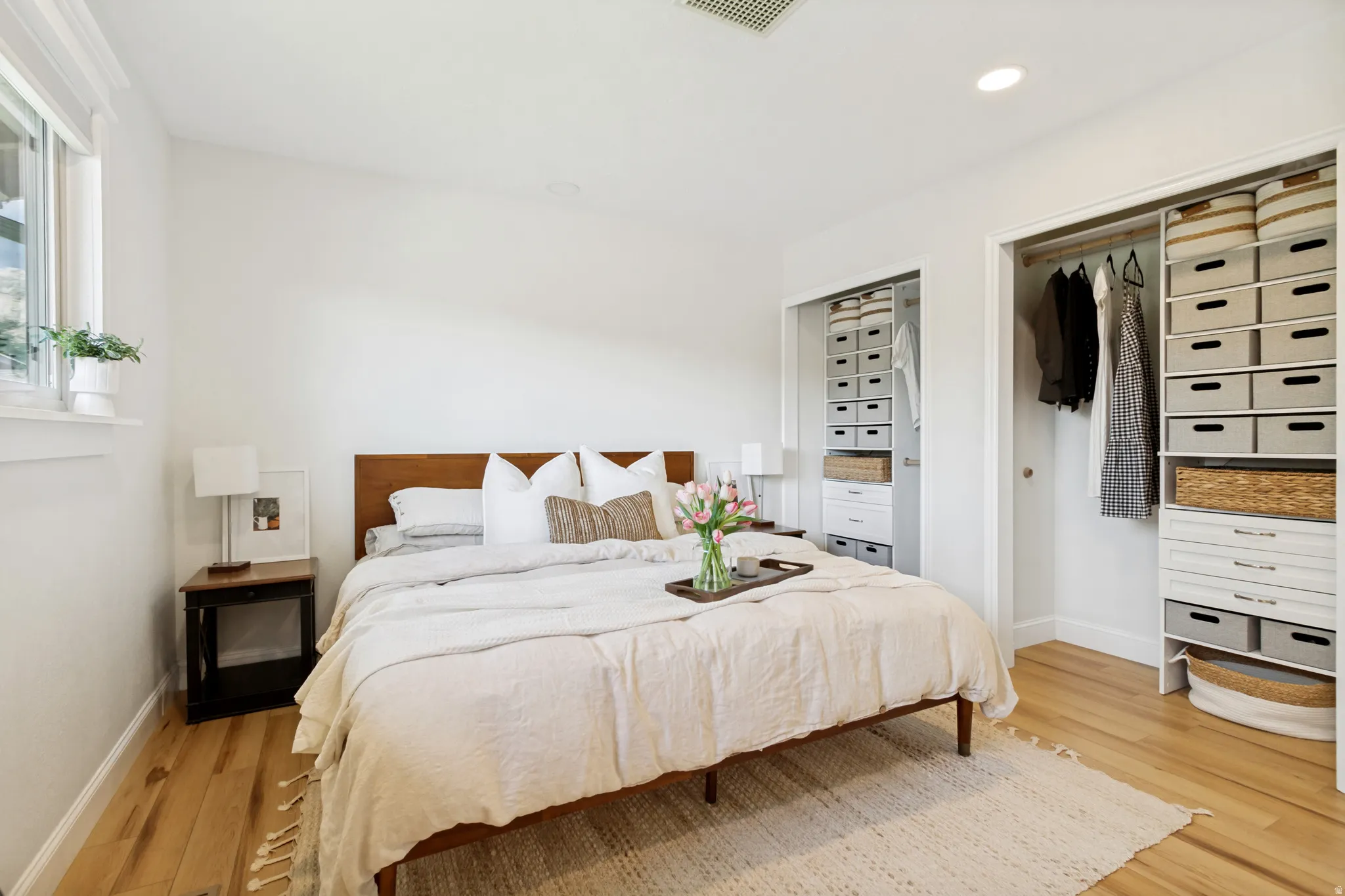 Bright bedroom featuring wood-finish flooring and two built-in closet systems
