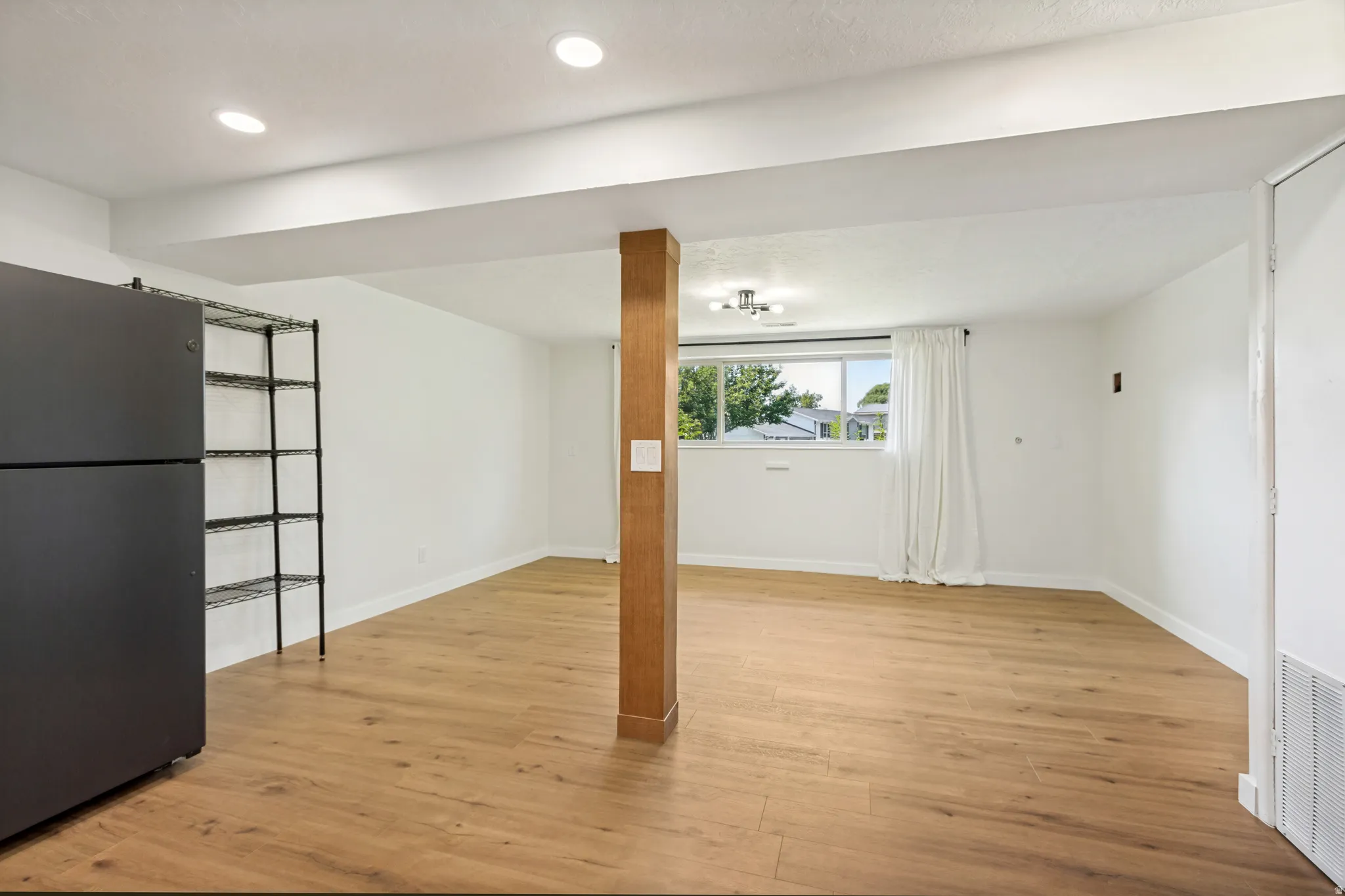 Spacious room featuring wood-finish flooring, white walls, and a visible window for natural light